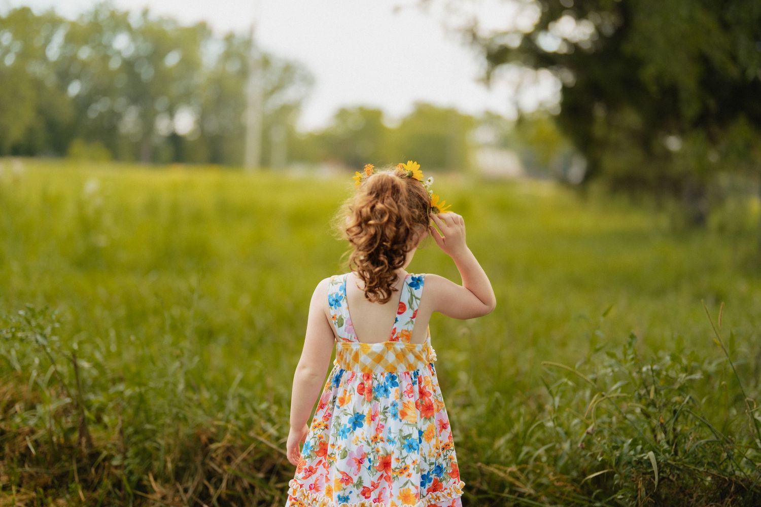 A girl in a floral dress stands in a sunny meadow looking into the distance. fremont, ohio