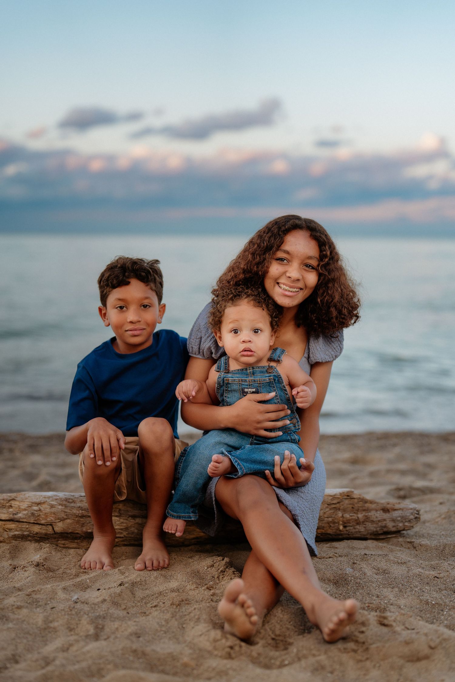 Children sitting together on a beach at sunset with the ocean and cloudy sky in the background. Huron Ohio Beach