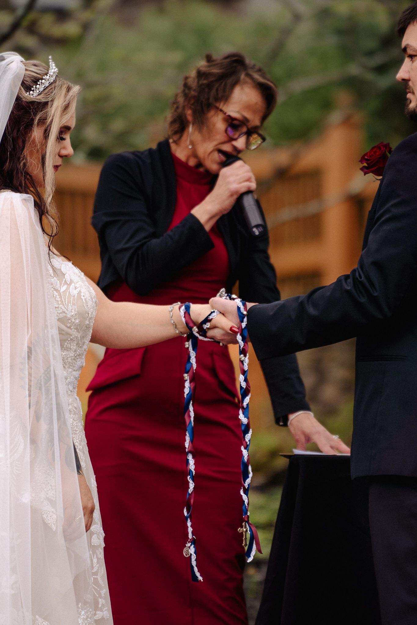 Officiant performs handfasting ceremony tying colorful ribbon around bride and groom hands at outdoor wedding.