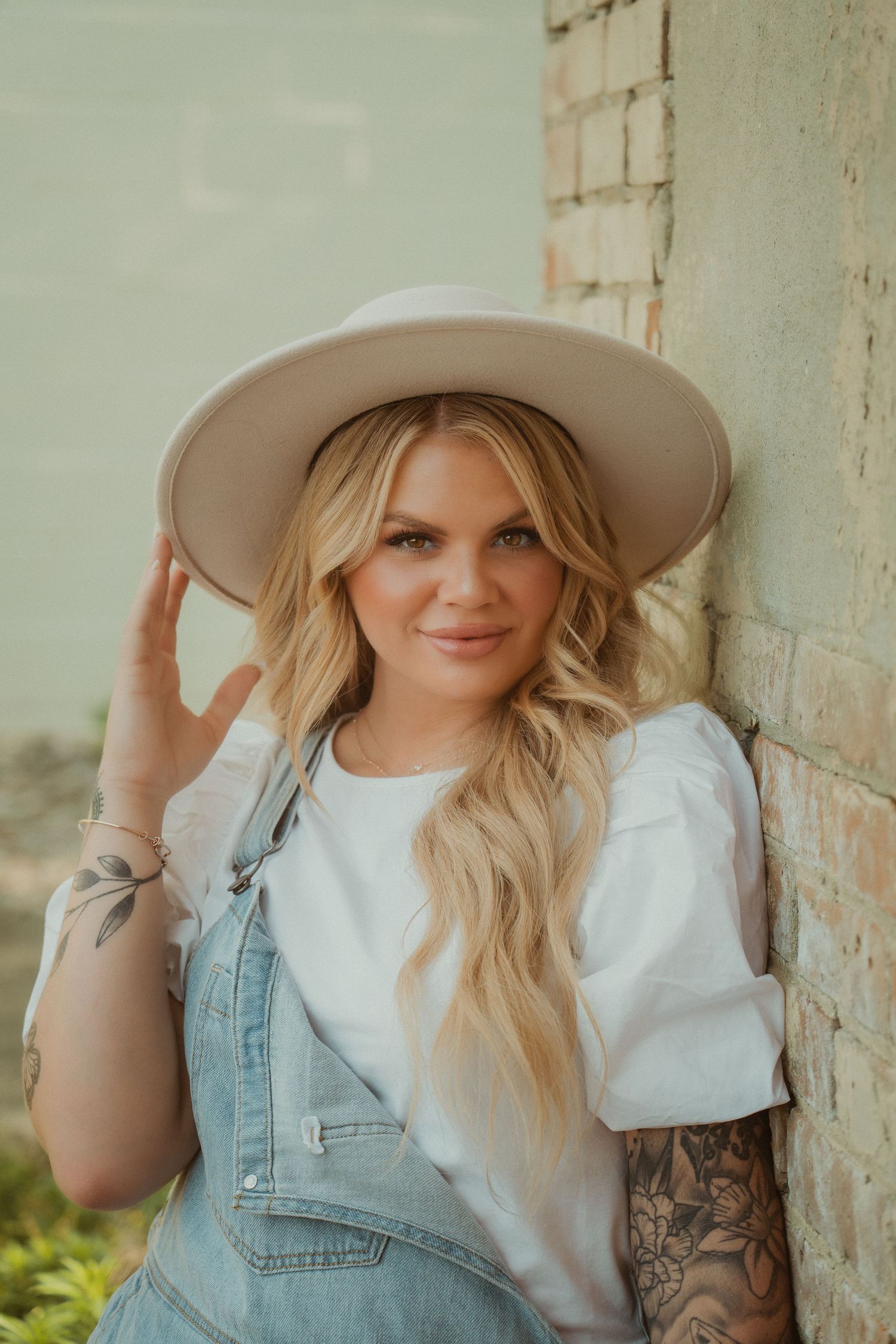 Fashion portrait with wide brim hat, white top and denim against rustic wall. Fremont, Ohio Hair Salon