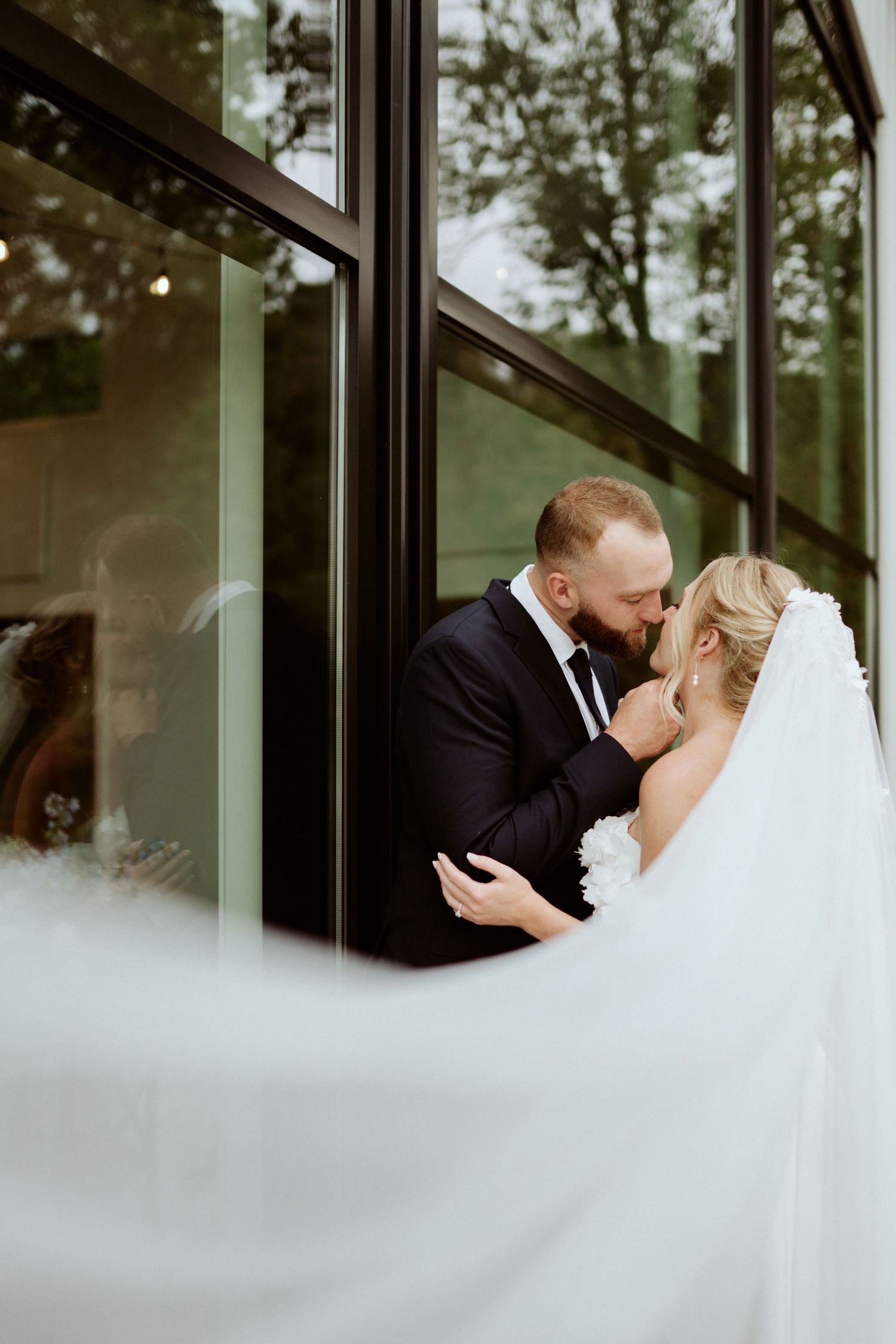 A wedding couple embraces near glass windows in an artistic sequence. Wooster Ohio The Wellspring Wedding Venue