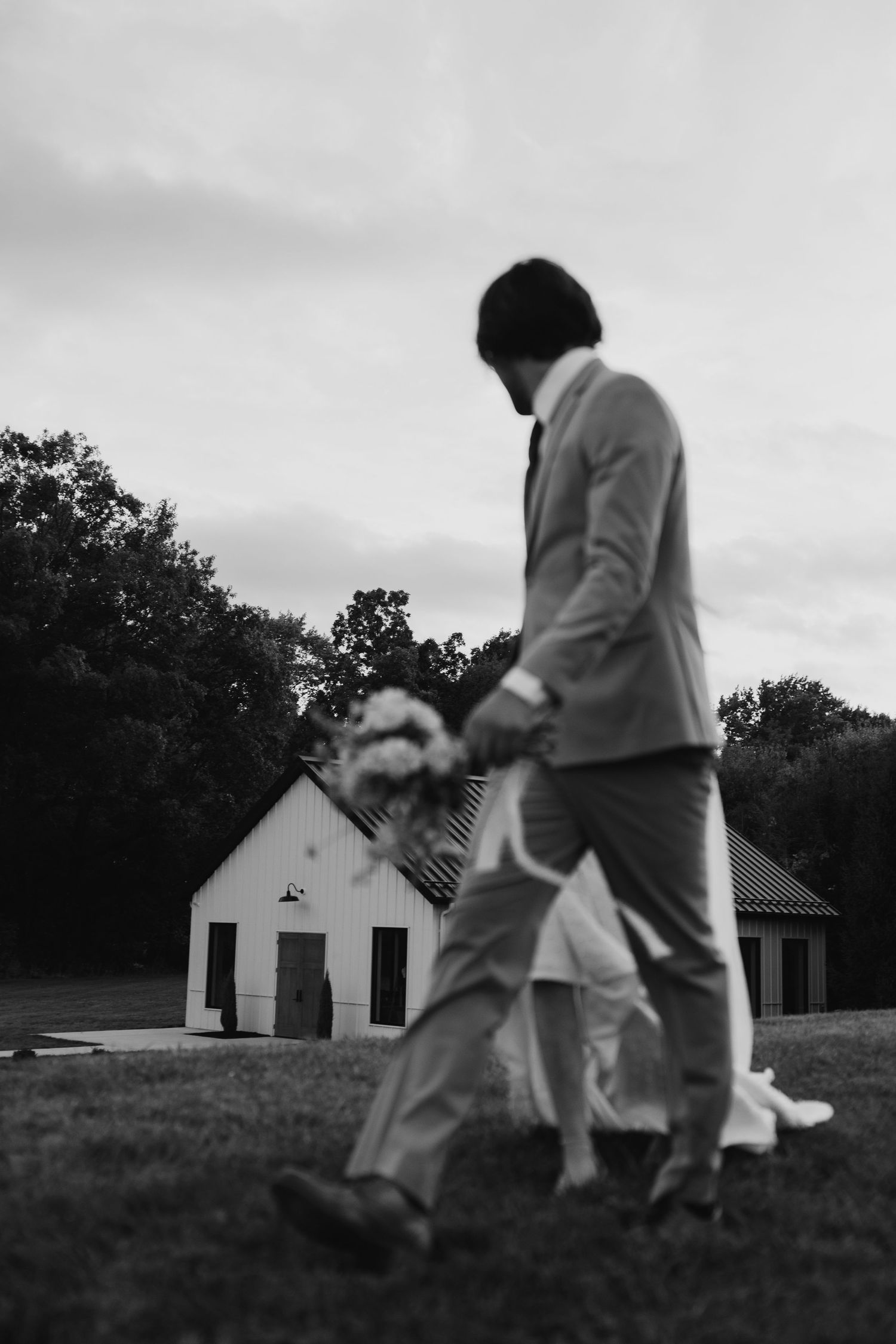 A black and white sequence of playful movement on a grassy hill near white buildings. Wooster Ohio The Wellspring Wedding Venue