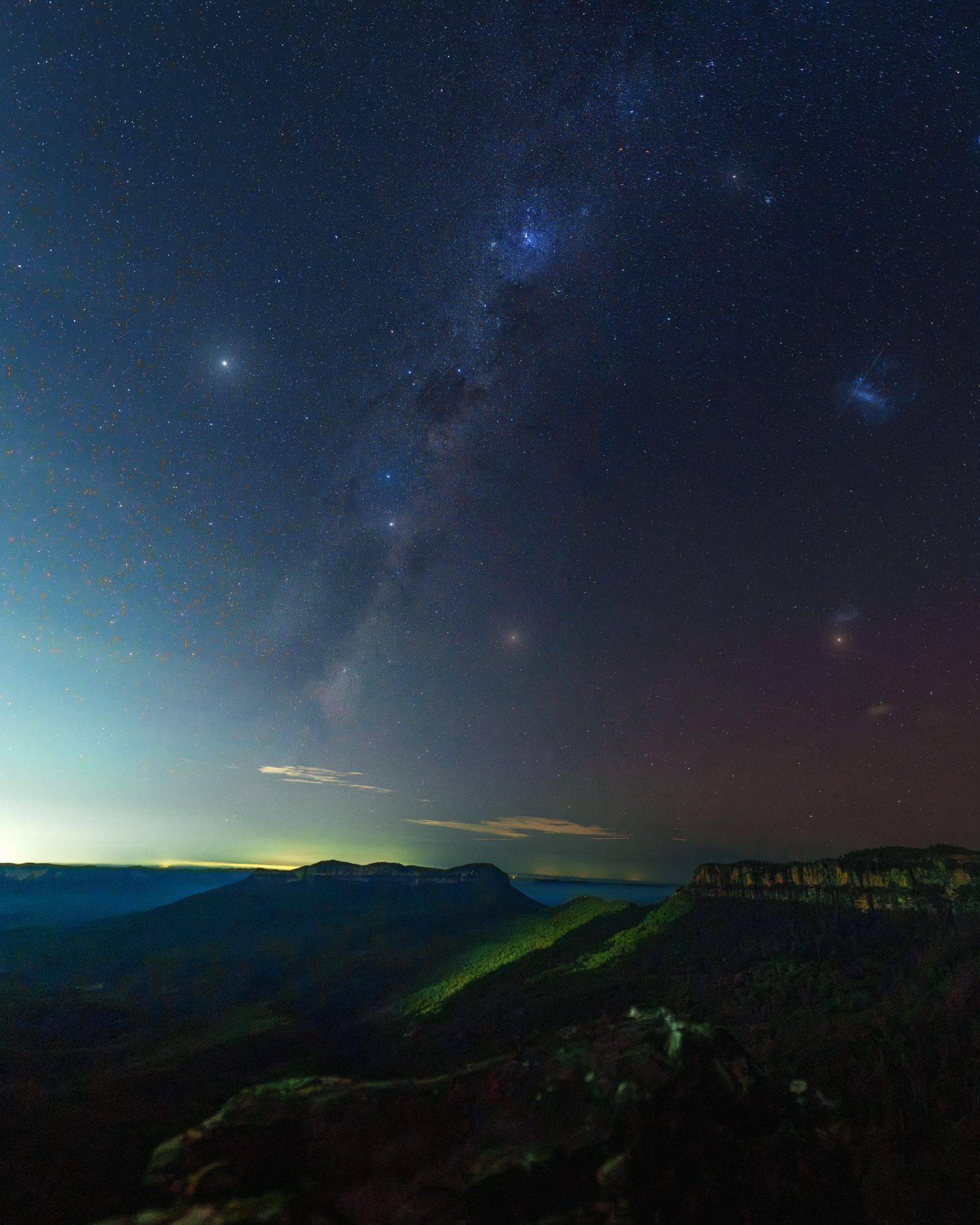 Milky Way galaxy arching over a dramatic canyon landscape at night with glowing horizon and star-filled sky.