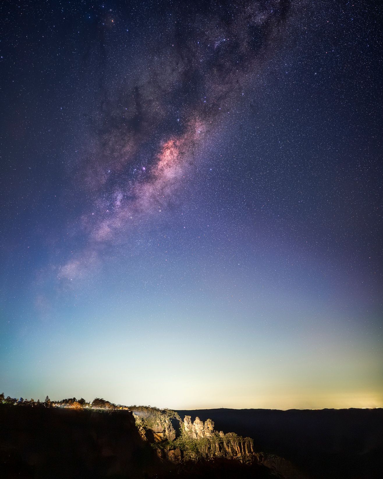 Milky Way galaxy stretches across the night sky above illuminated cliffs in a stunning landscape.