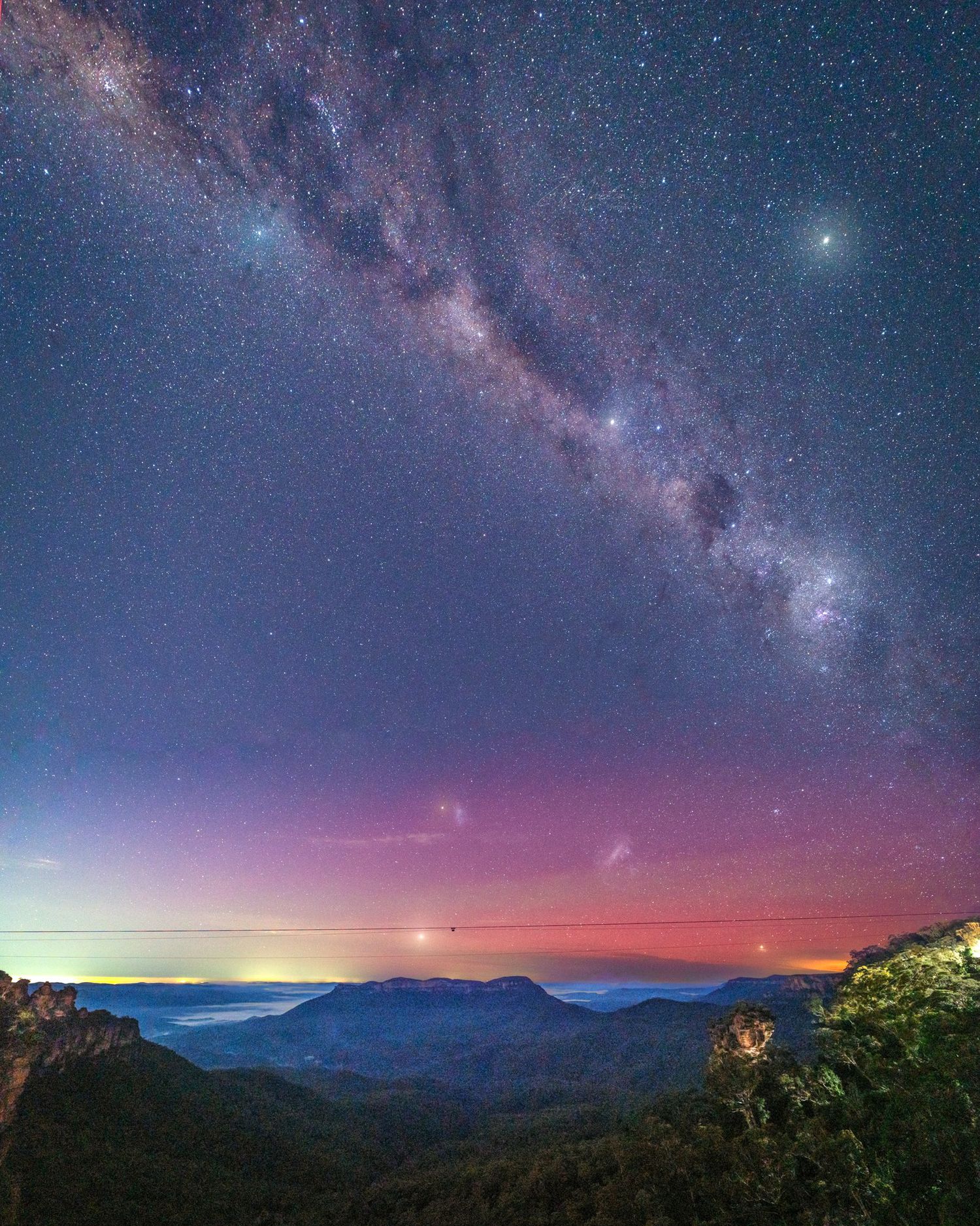 Stunning night sky panorama showing the Milky Way galaxy over mountain silhouettes at dawn.