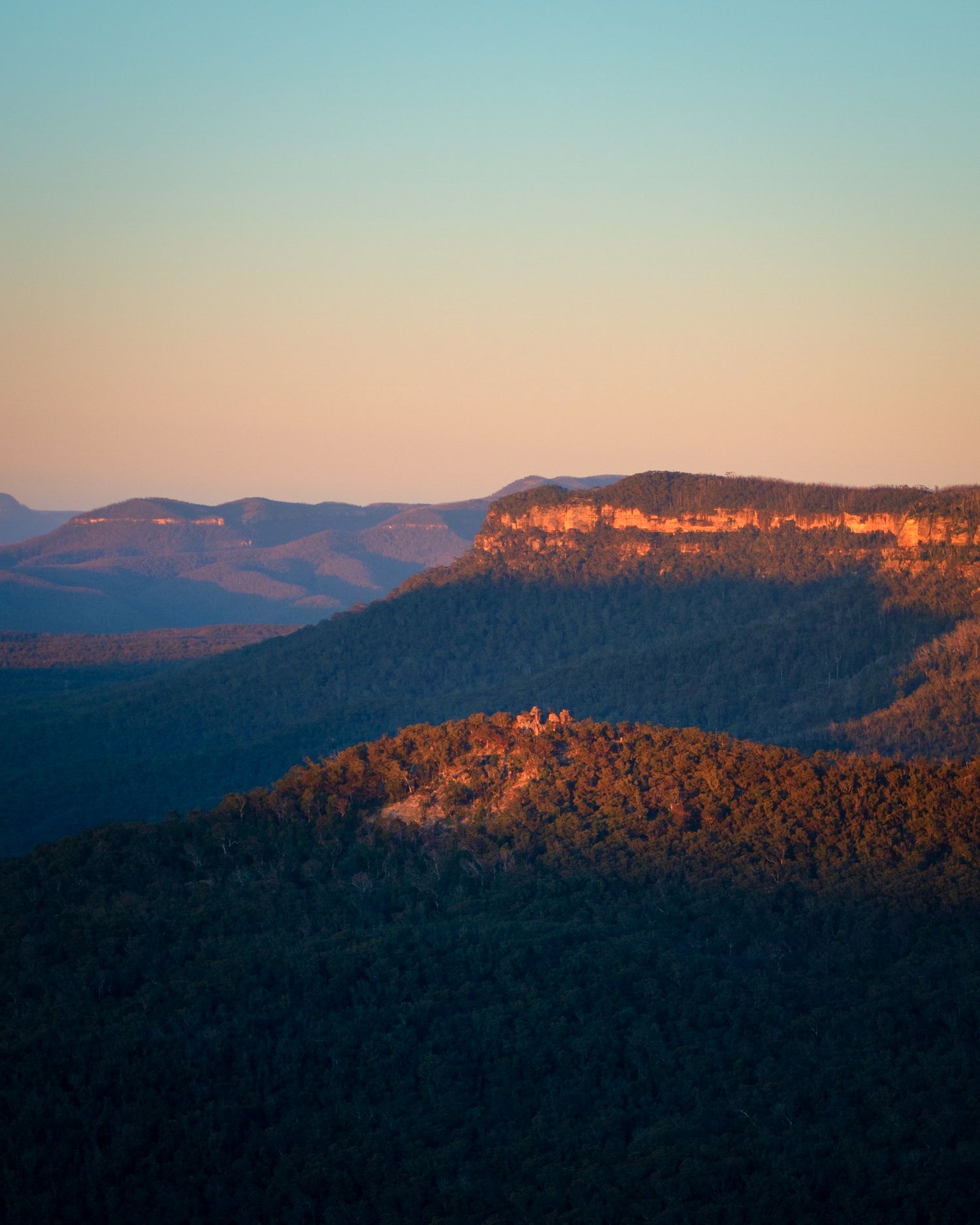Panoramic view of mountain ranges at sunset with golden cliffs and forested slopes.