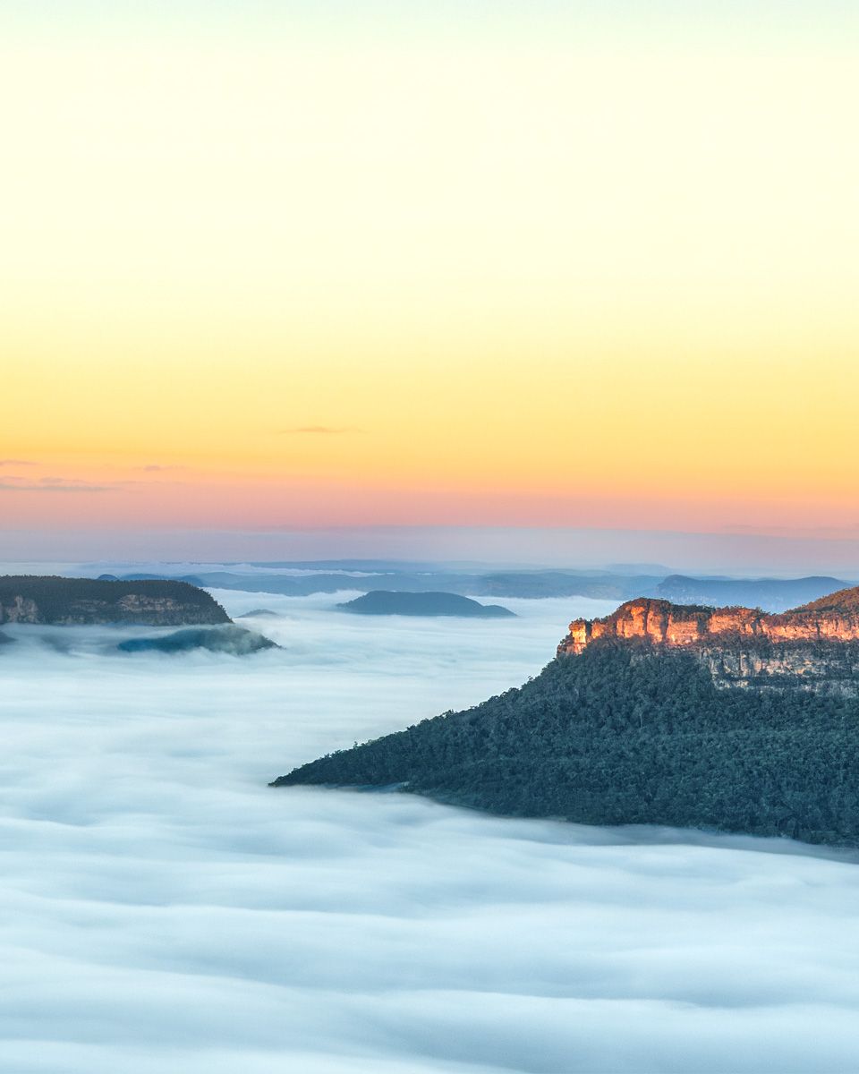 Stunning sunrise over Blue Mountains with misty clouds filling the valley, rocky peaks emerging above the fog.