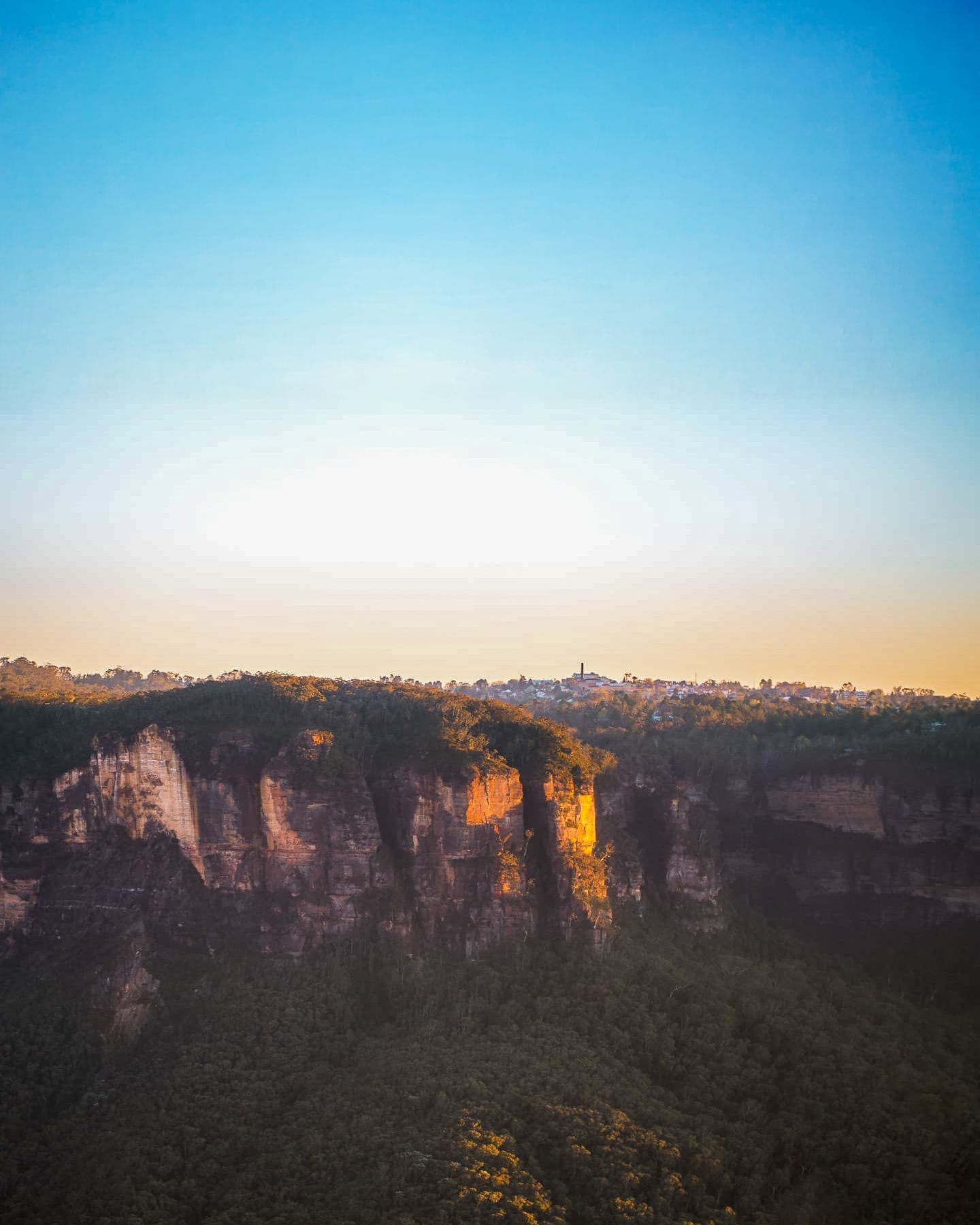 Panoramic view of sandstone cliffs and valleys in the Blue Mountains during golden hour.