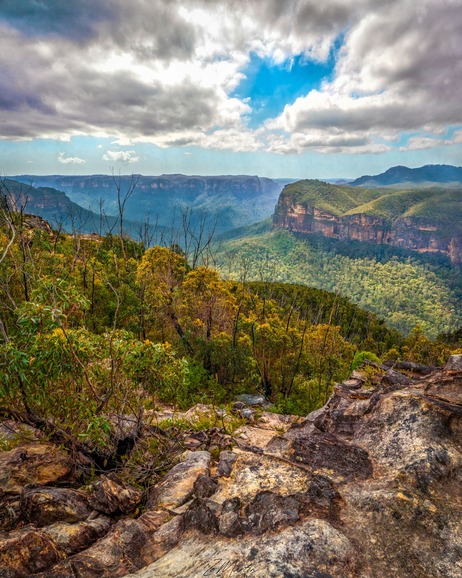 Dramatic cliffs and valleys of the Blue Mountains in Australia with sunlit clouds and lush vegetation.