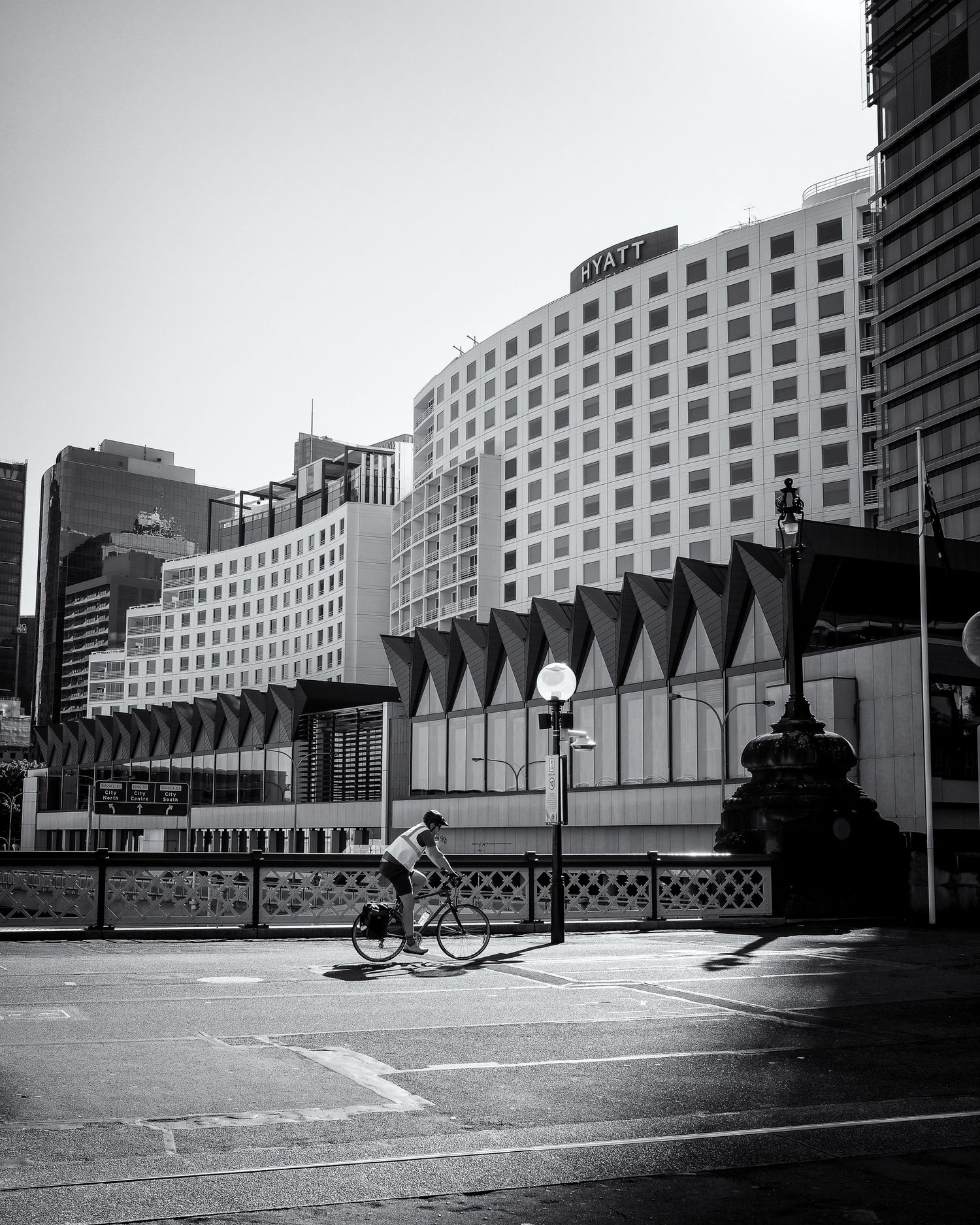 Black and white urban street photo of a cyclist riding past the Hyatt hotel and modern buildings in a city.