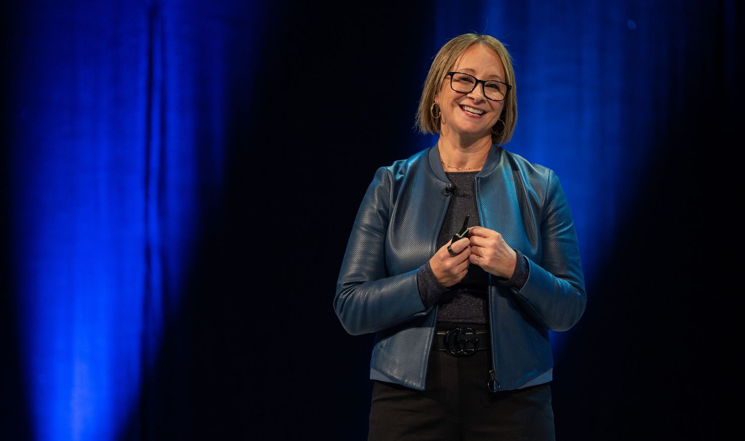 Speaker on stage with dramatic blue lighting delivering presentation at business conference.
