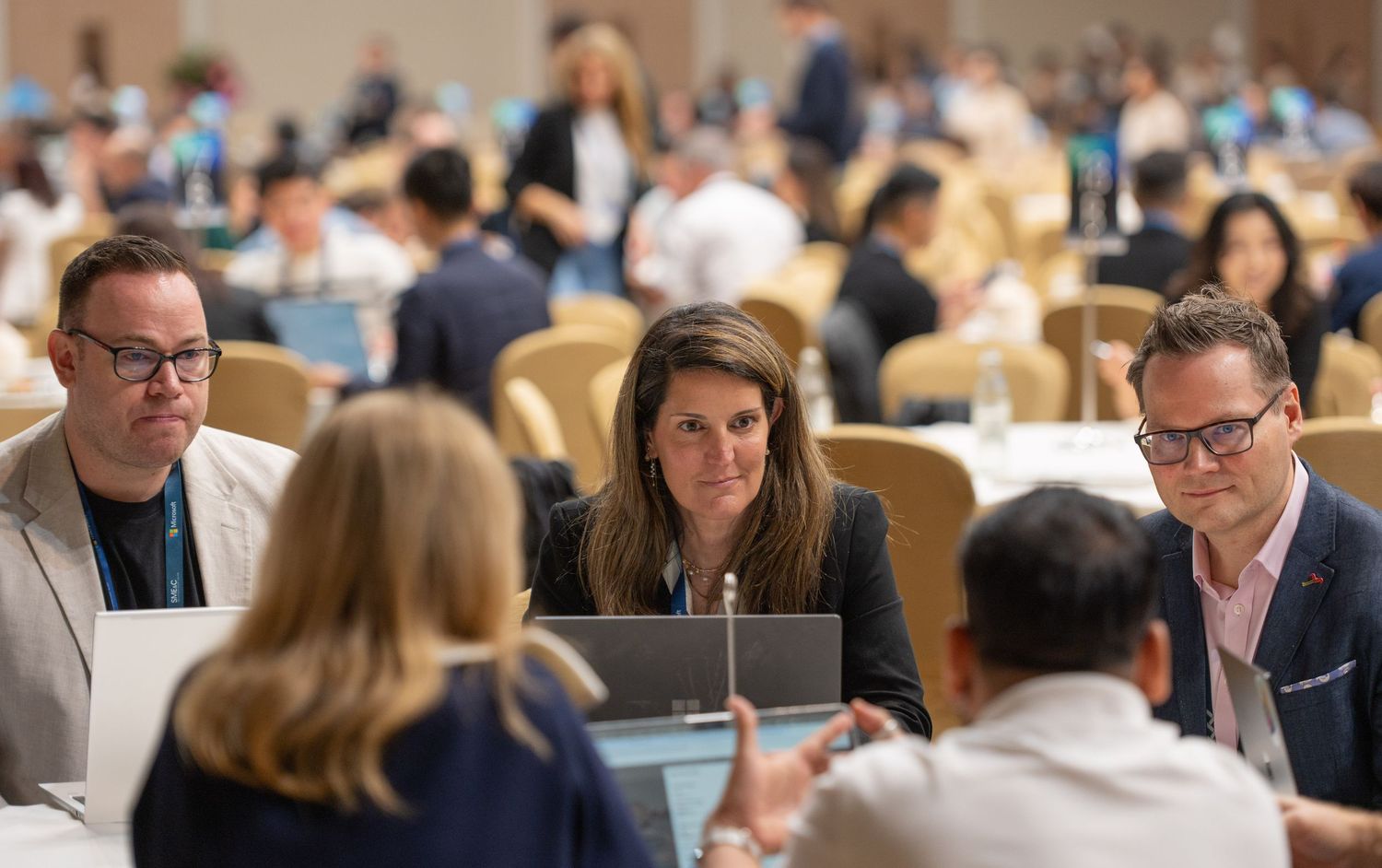 Business professionals seated at round tables during conference breakout session.