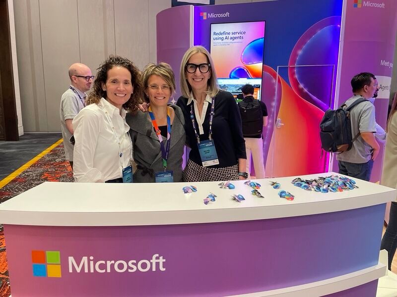 Group of attendees posing at Microsoft branded booth display with promotional materials.
