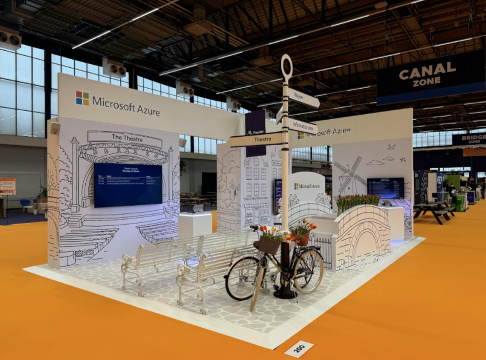 Panoramic view of a modern tech exhibition space with white displays and orange accents in a large convention hall.