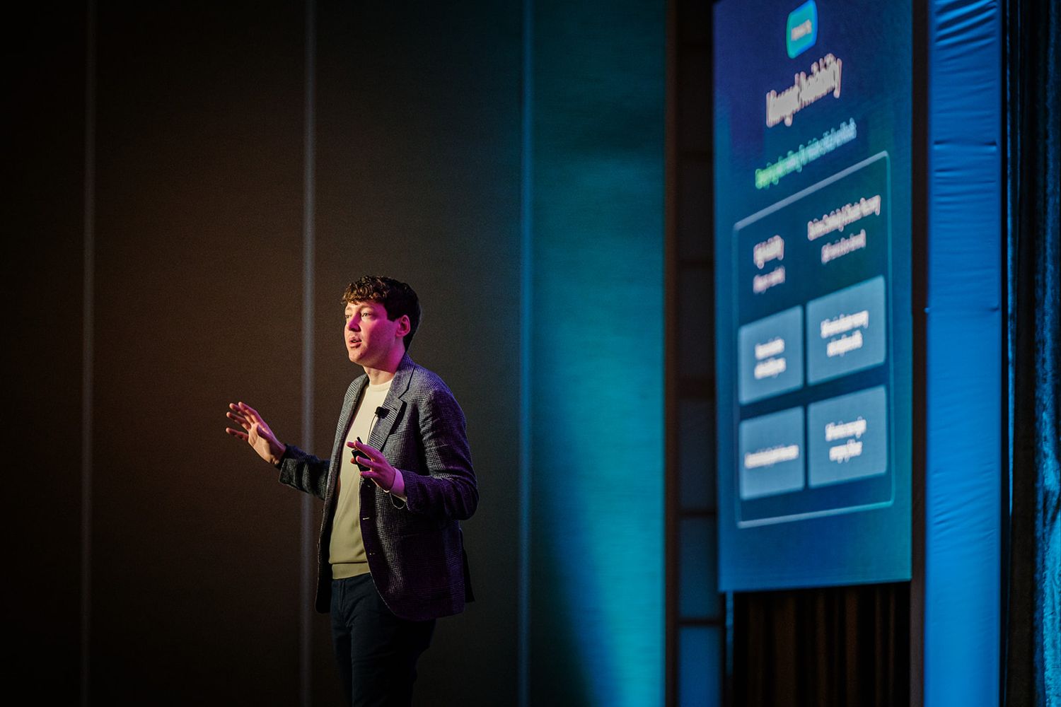 Business presentation being delivered on stage with corporate branding and blue ambient lighting.