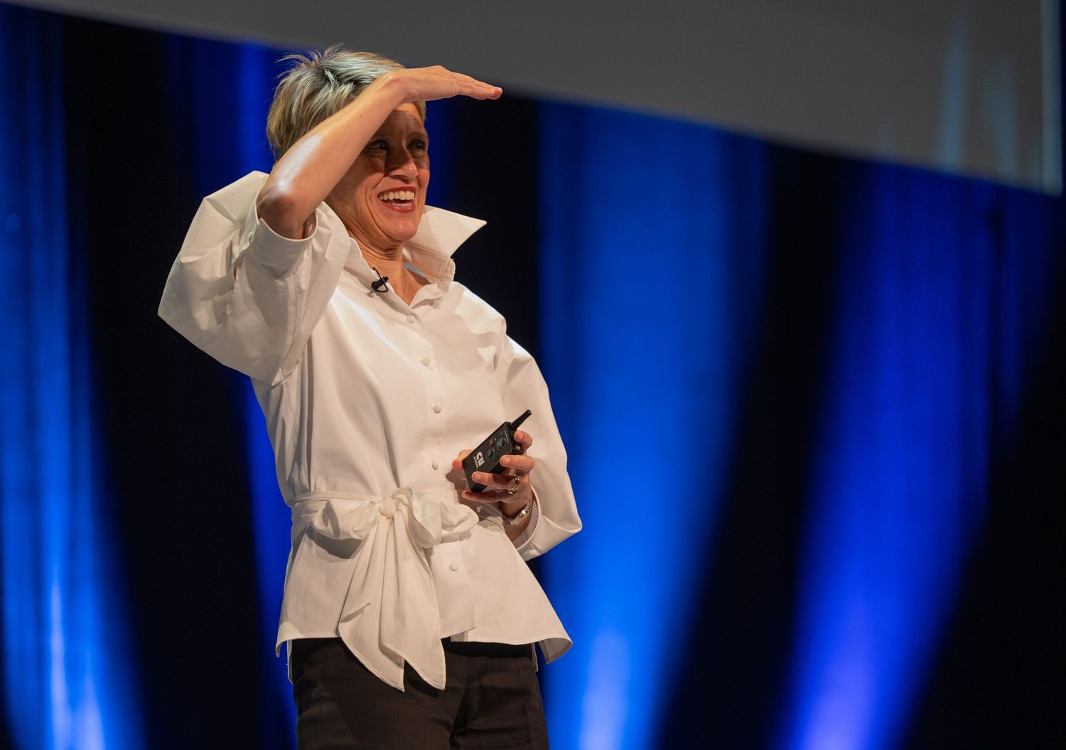 Animated speaker in white shirt gesturing energetically against blue stage lighting.