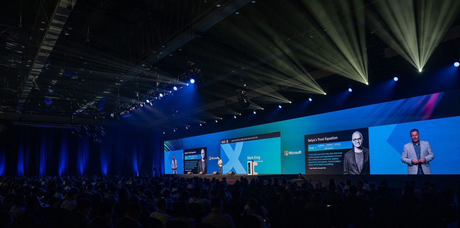 Modern conference venue with blue and purple lighting illuminating white chairs and staging area.