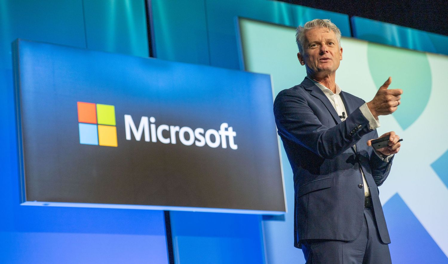 Microsoft corporate presentation stage with speaker and blue branded backdrop.