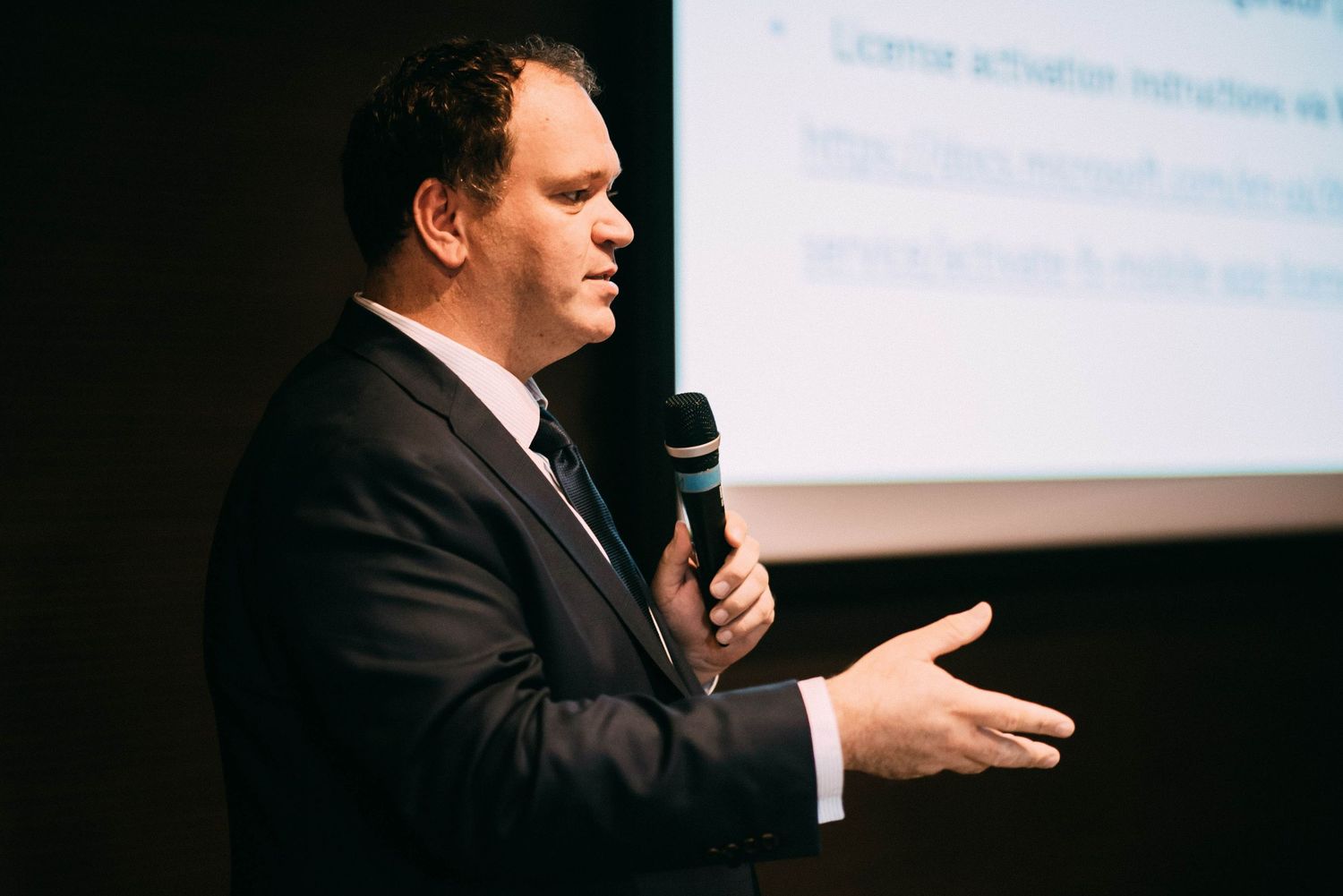Speaker presenting on stage at technology conference with dark background.