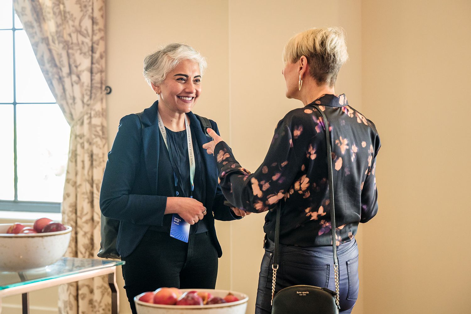 Two people sharing a warm conversation in a bright interior room with fruit on the table.