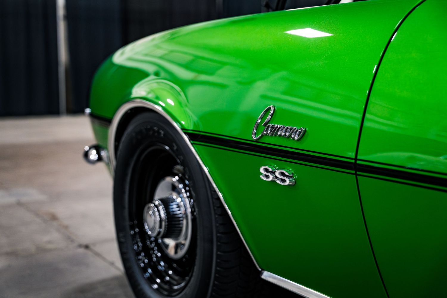 Close-up of a vibrant green Chevrolet Camaro SS muscle car showcasing its iconic badge and black spoke wheel.