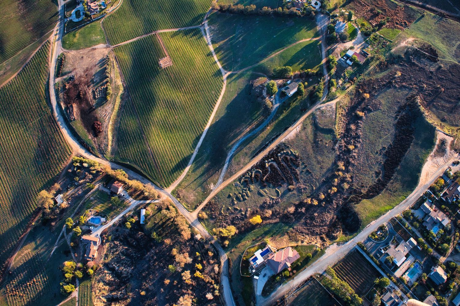 Aerial view of winding paths and green spaces in a rural landscape with scattered buildings.