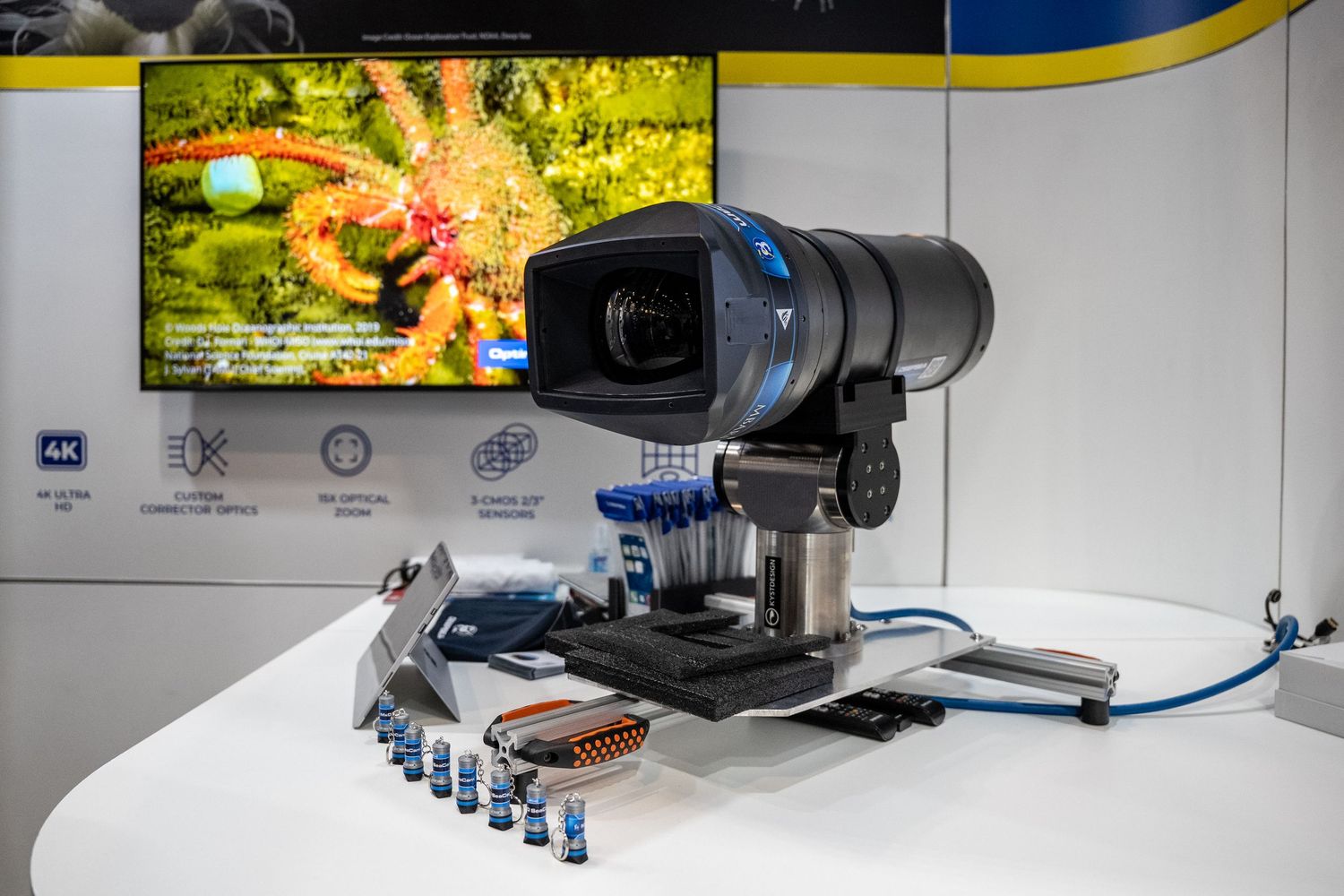Advanced 4K camera mounted on a microscope display at a tech exhibition with a colorful sea creature on screen.