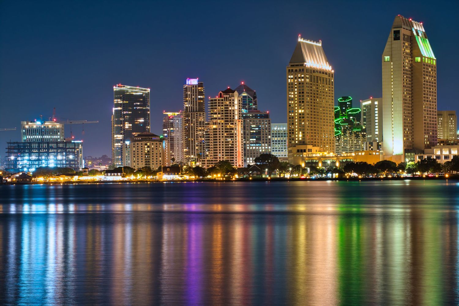 Panoramic nighttime skyline of San Diego with colorful reflections on the bay.