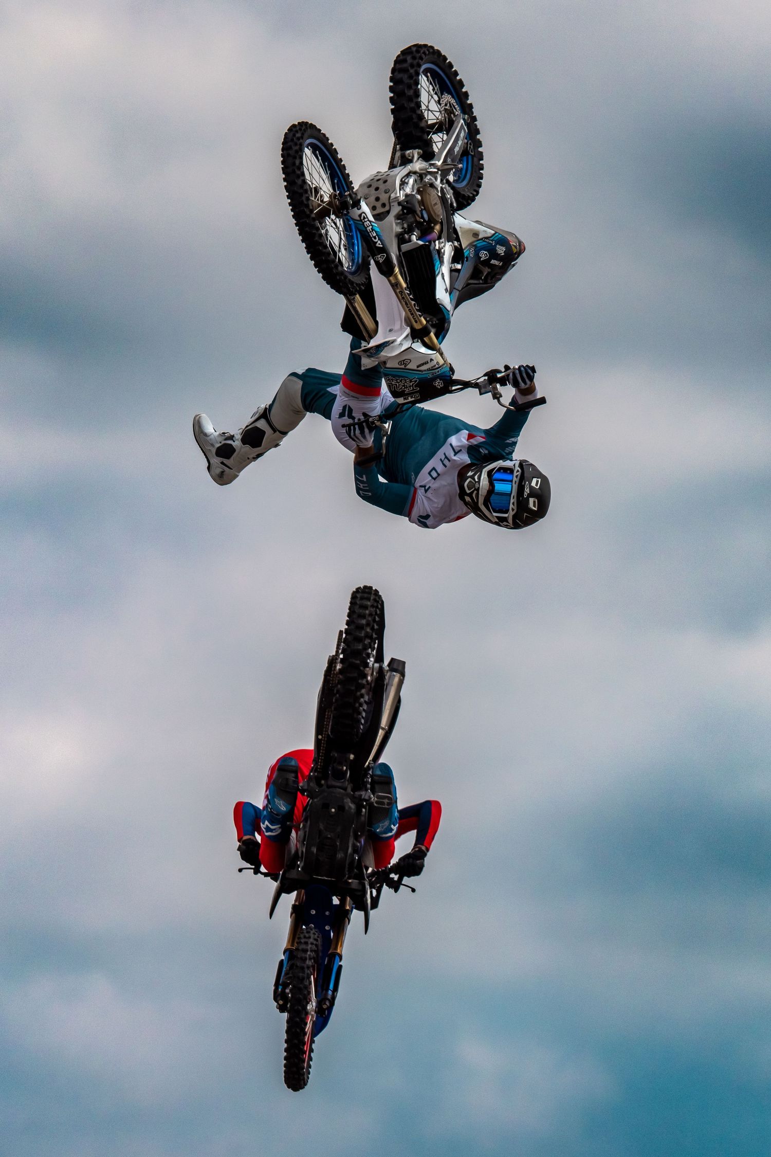 Two motocross riders performing synchronized backflips during an aerial stunt show.