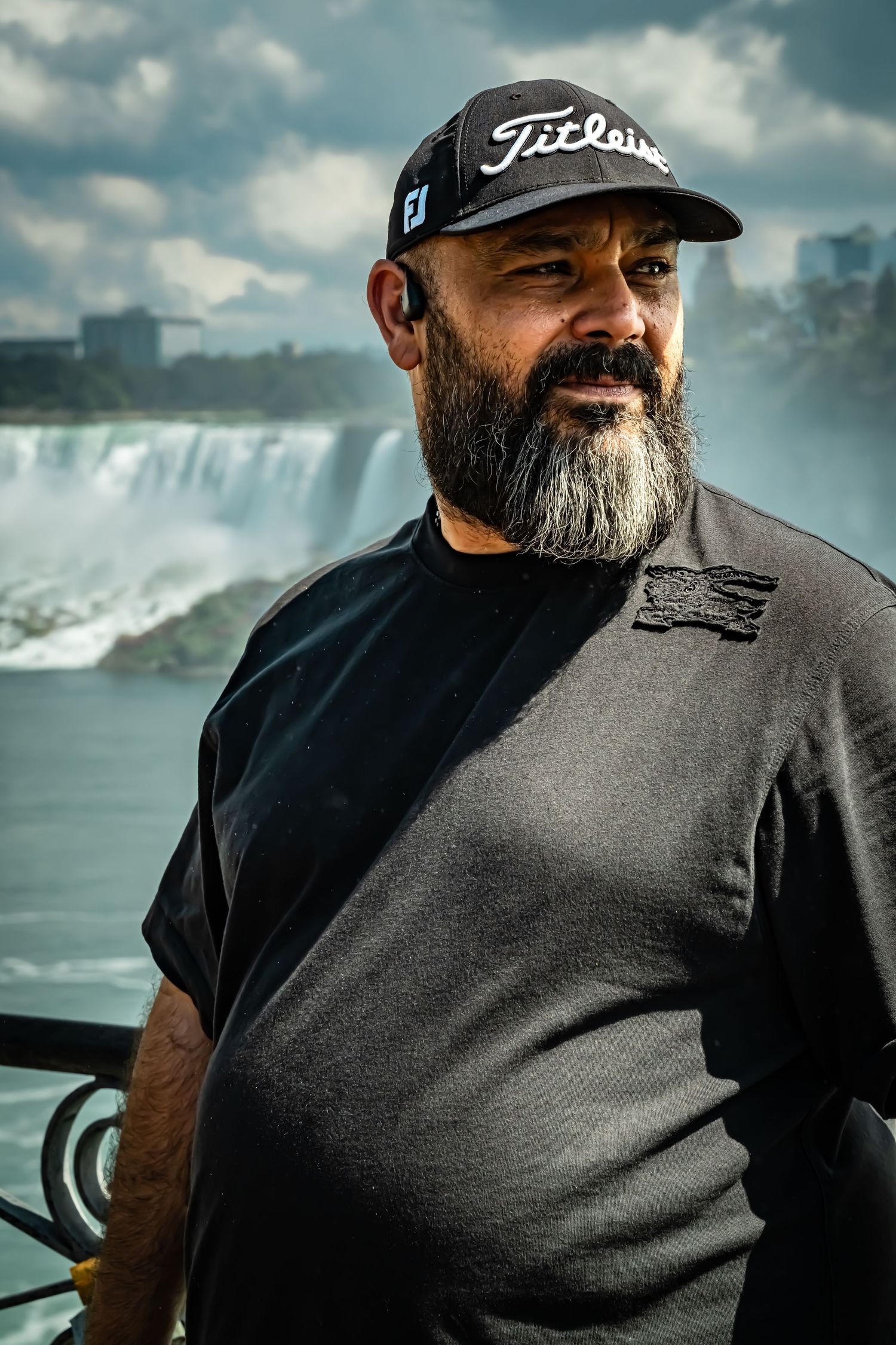 Bearded man in dark clothing and baseball cap smiling near a waterfall.