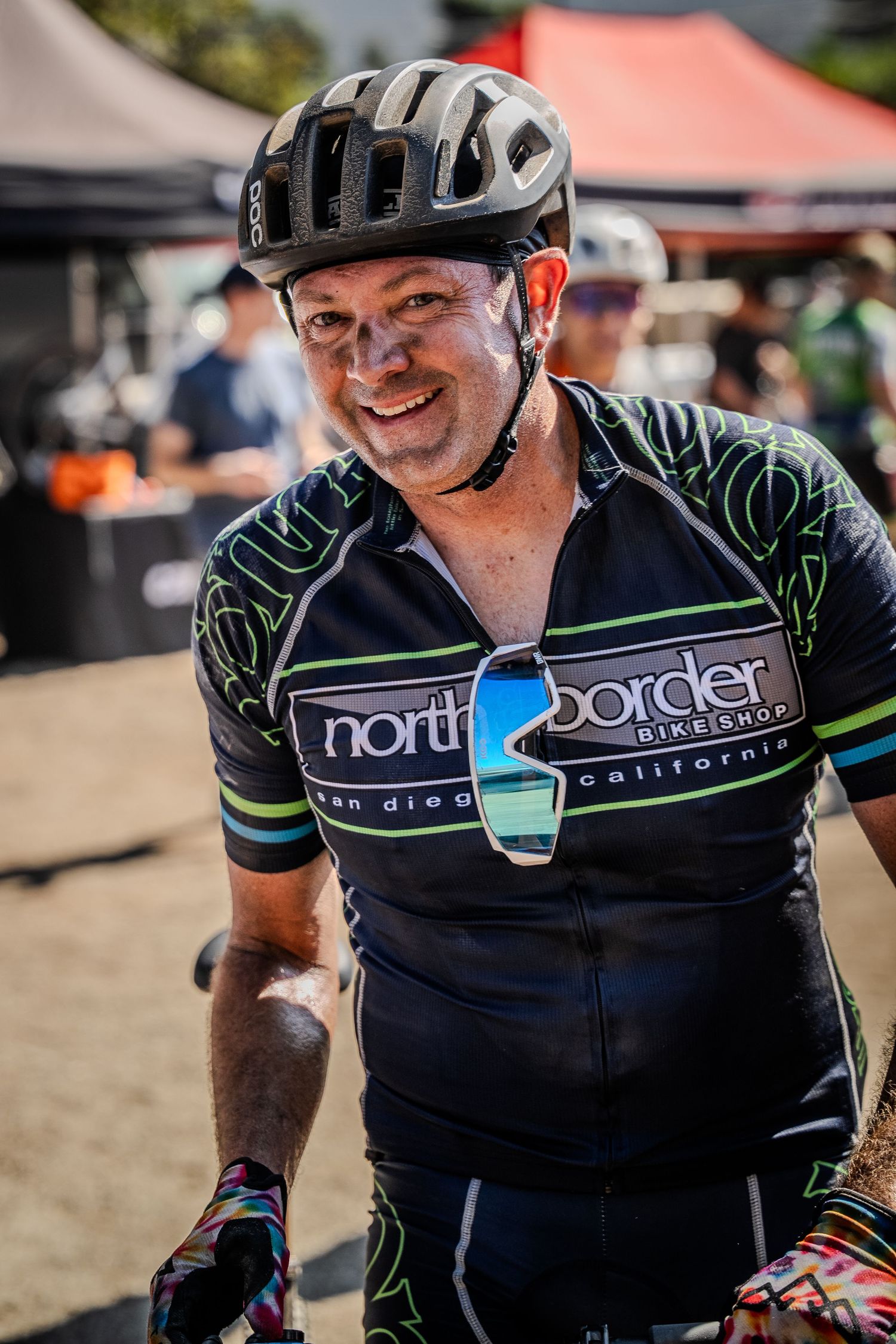 Cyclist wearing a black North Border cycling jersey and helmet smiling during an outdoor event.