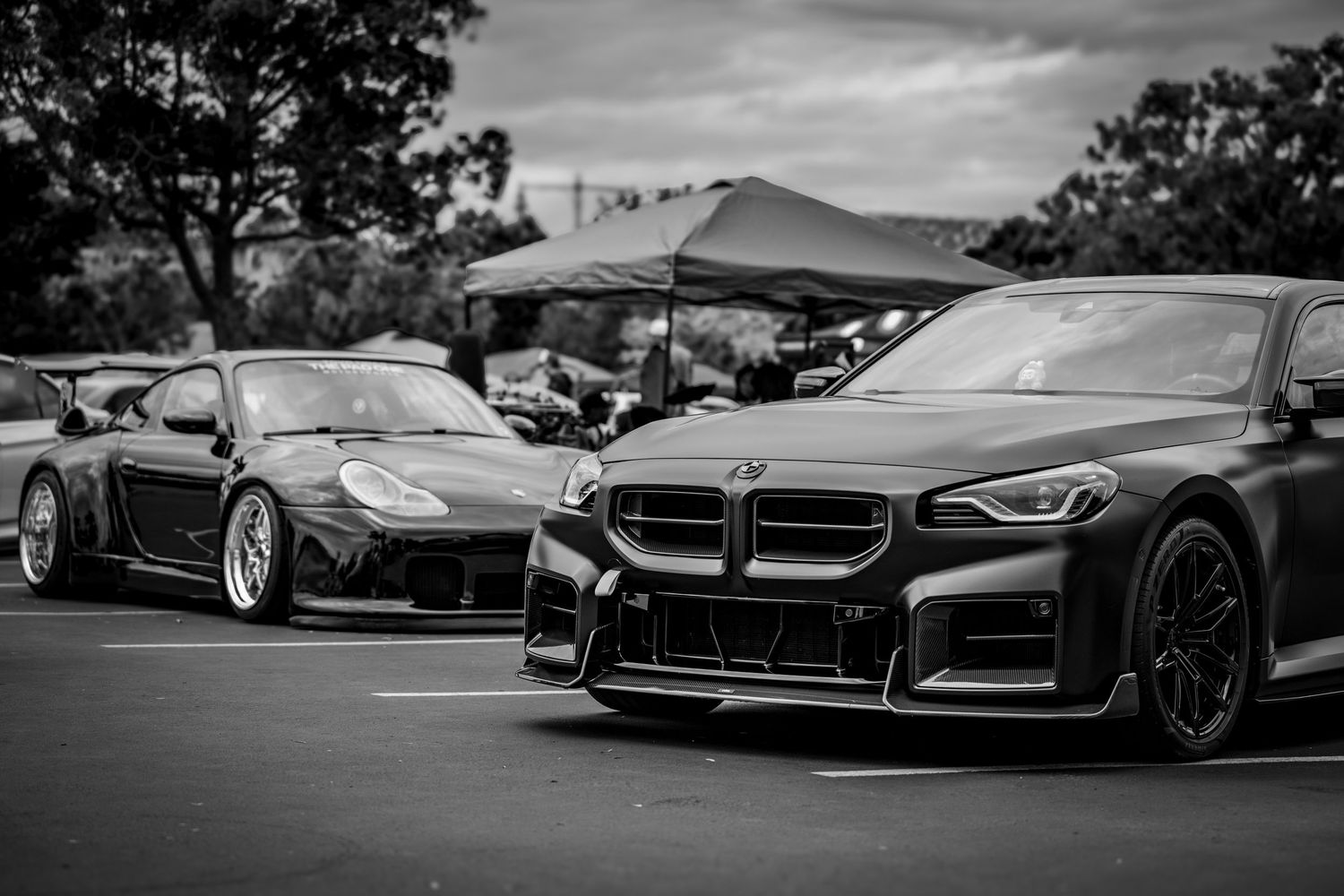 Black and white photograph of luxury sports cars parked in a row at an event.