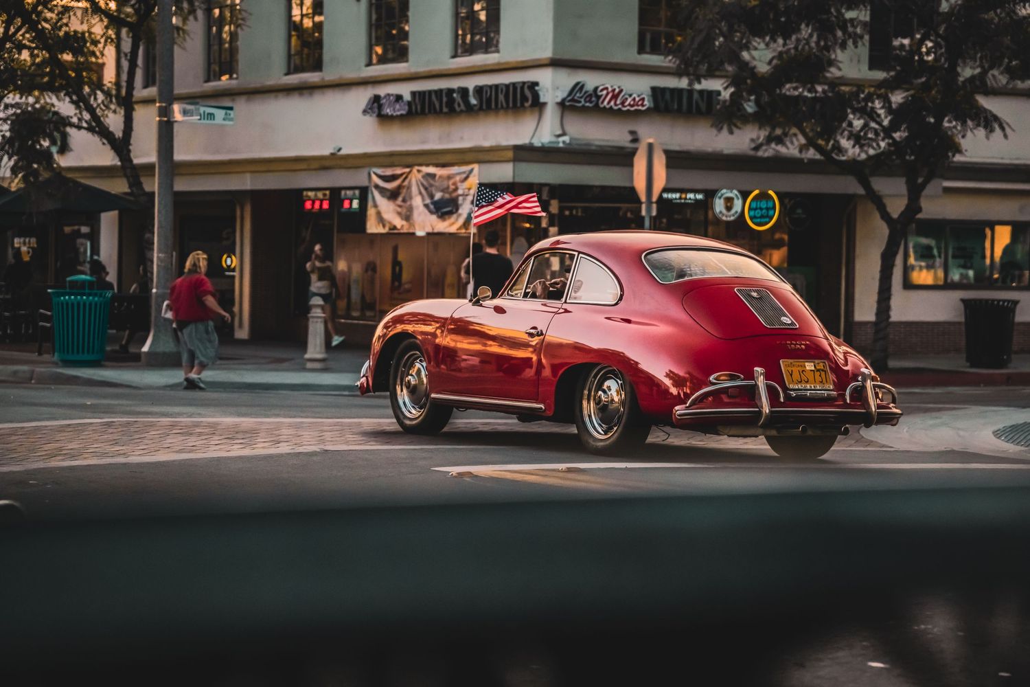 Vintage red Porsche 356 driving through city streets at sunset.