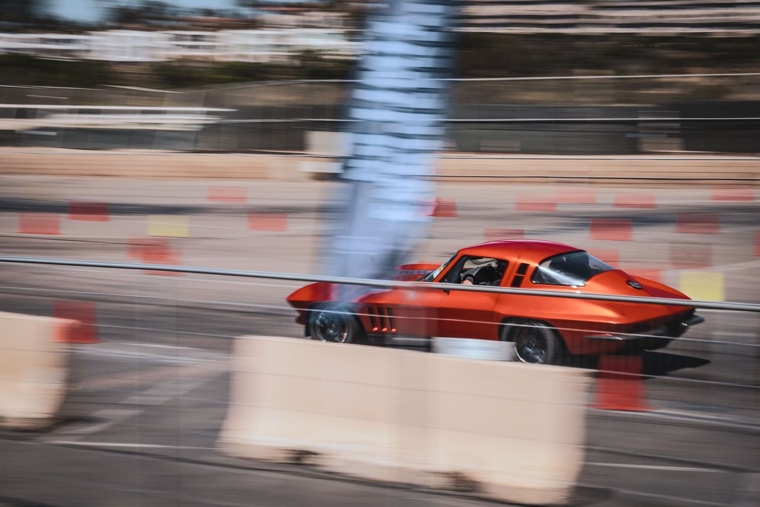 Vintage red race car speeding past concrete barriers on track.