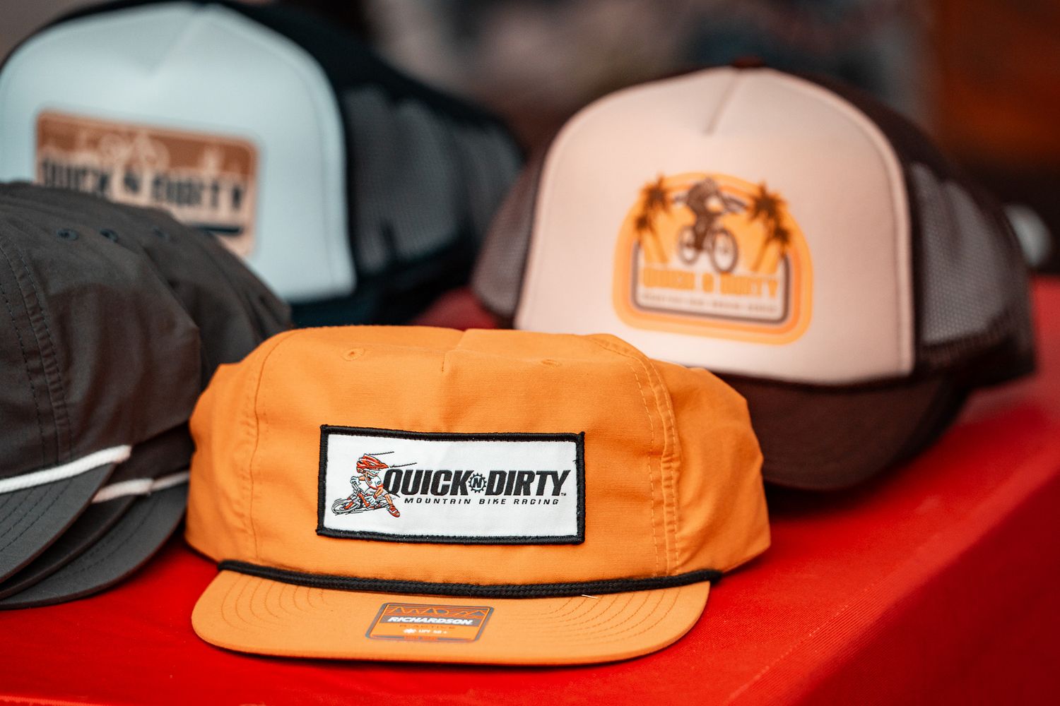 Orange and white branded baseball caps displayed on red surface.
