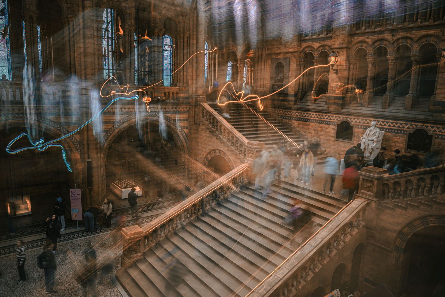 Person with umbrella walking through a dimly lit train station with dramatic architecture and staircase in the background.
