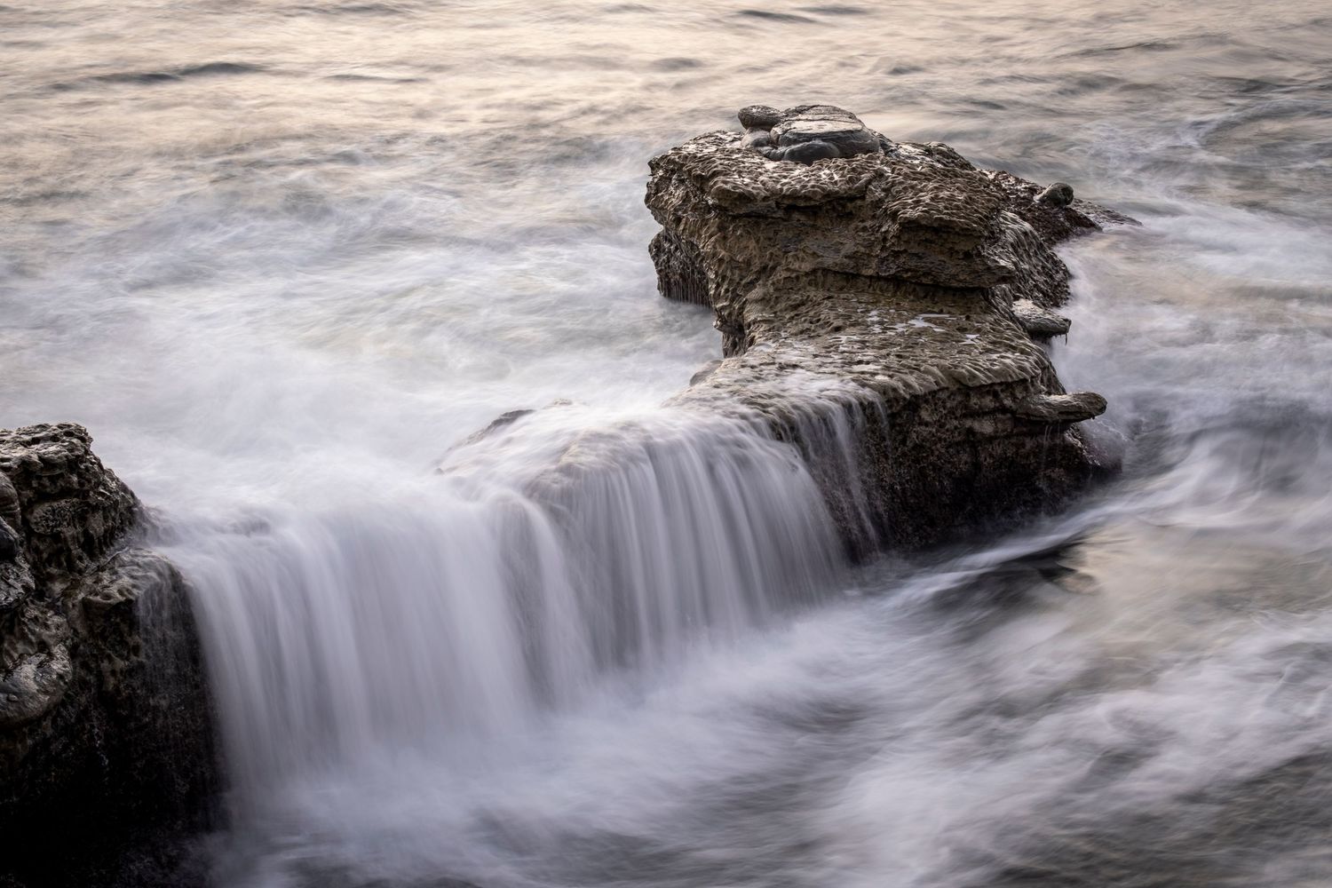 Long exposure of ocean waves flowing over coastal rocks creating smooth water effects.
