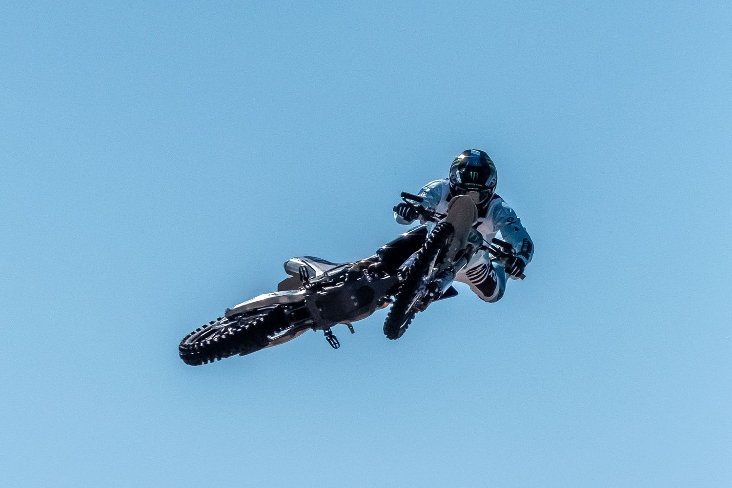 Sequence of motocross bike jumps against blue sky.