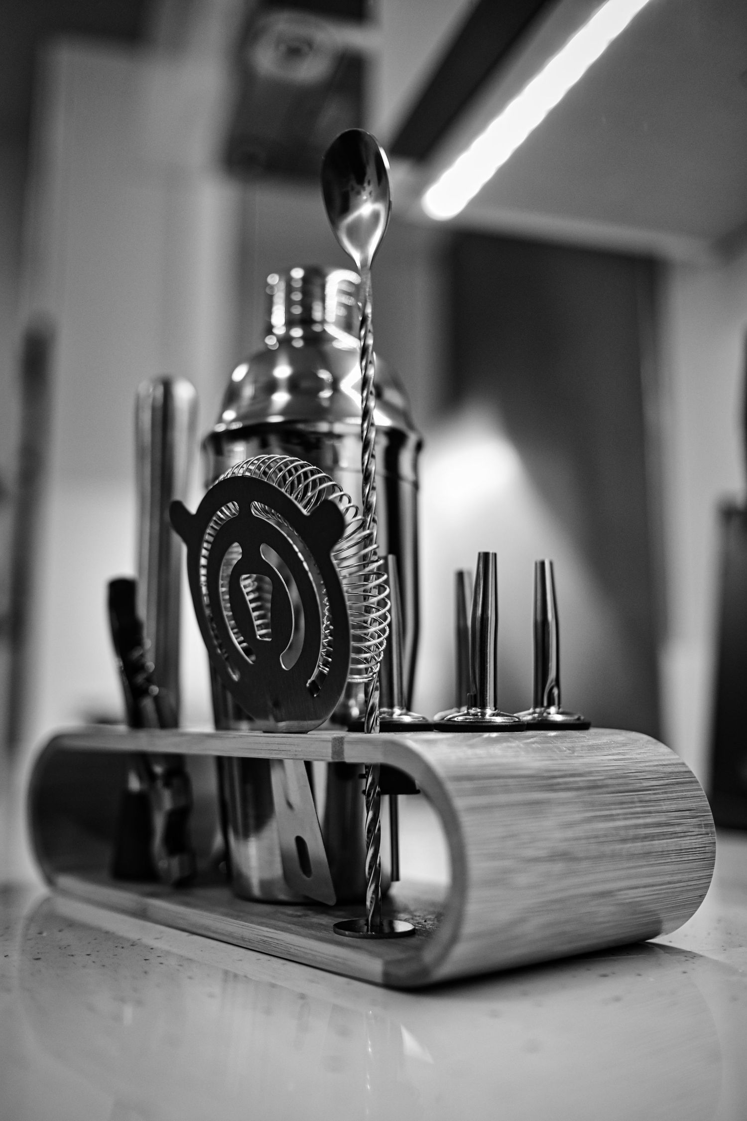 Black and white photo of a cocktail mixing station with bottles and bar tools.