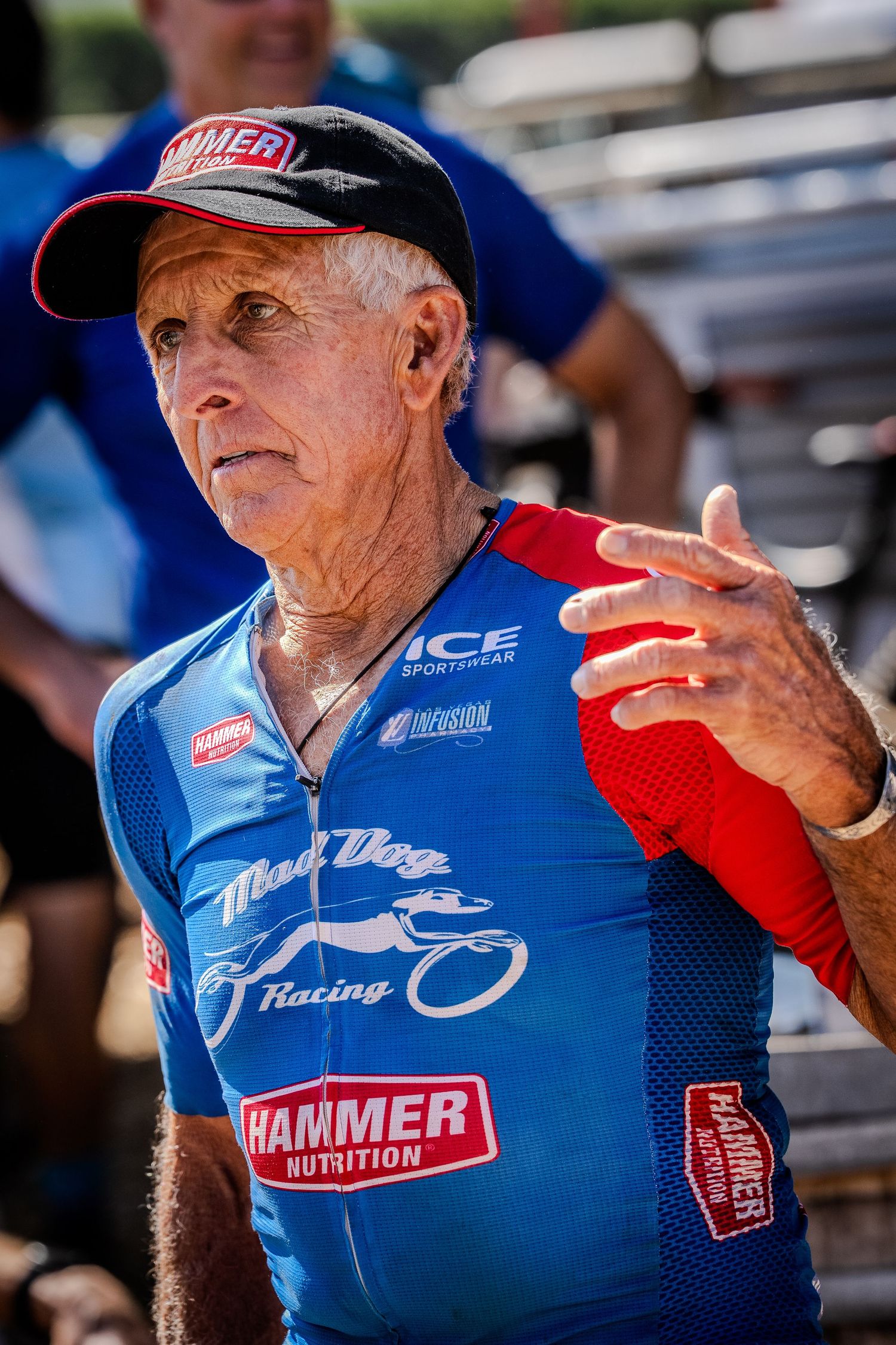 Senior athlete in blue racing jersey making hand gestures outdoors.