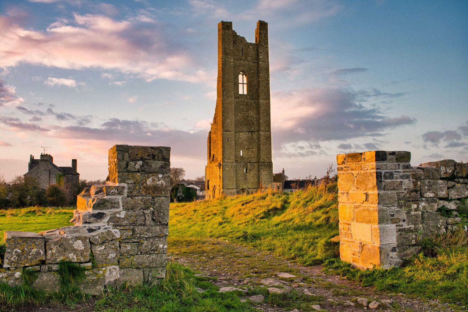 Ancient stone tower ruins against a dramatic sunset sky in an Irish countryside.