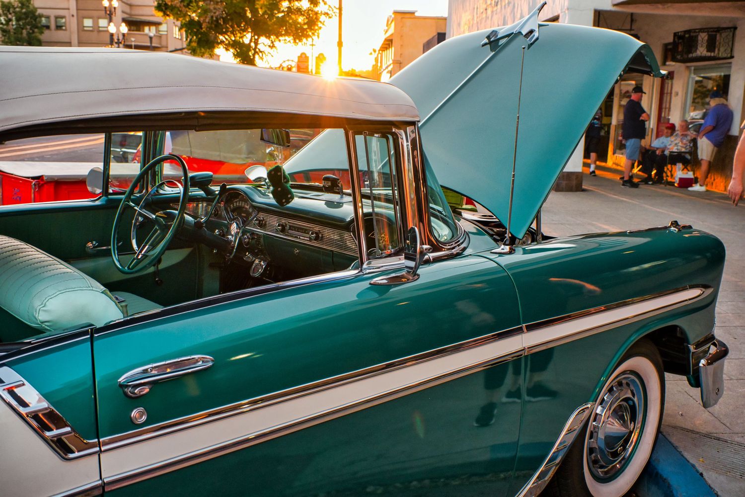 Classic teal-colored vintage car with chrome trim and white wall tires parked at sunset.