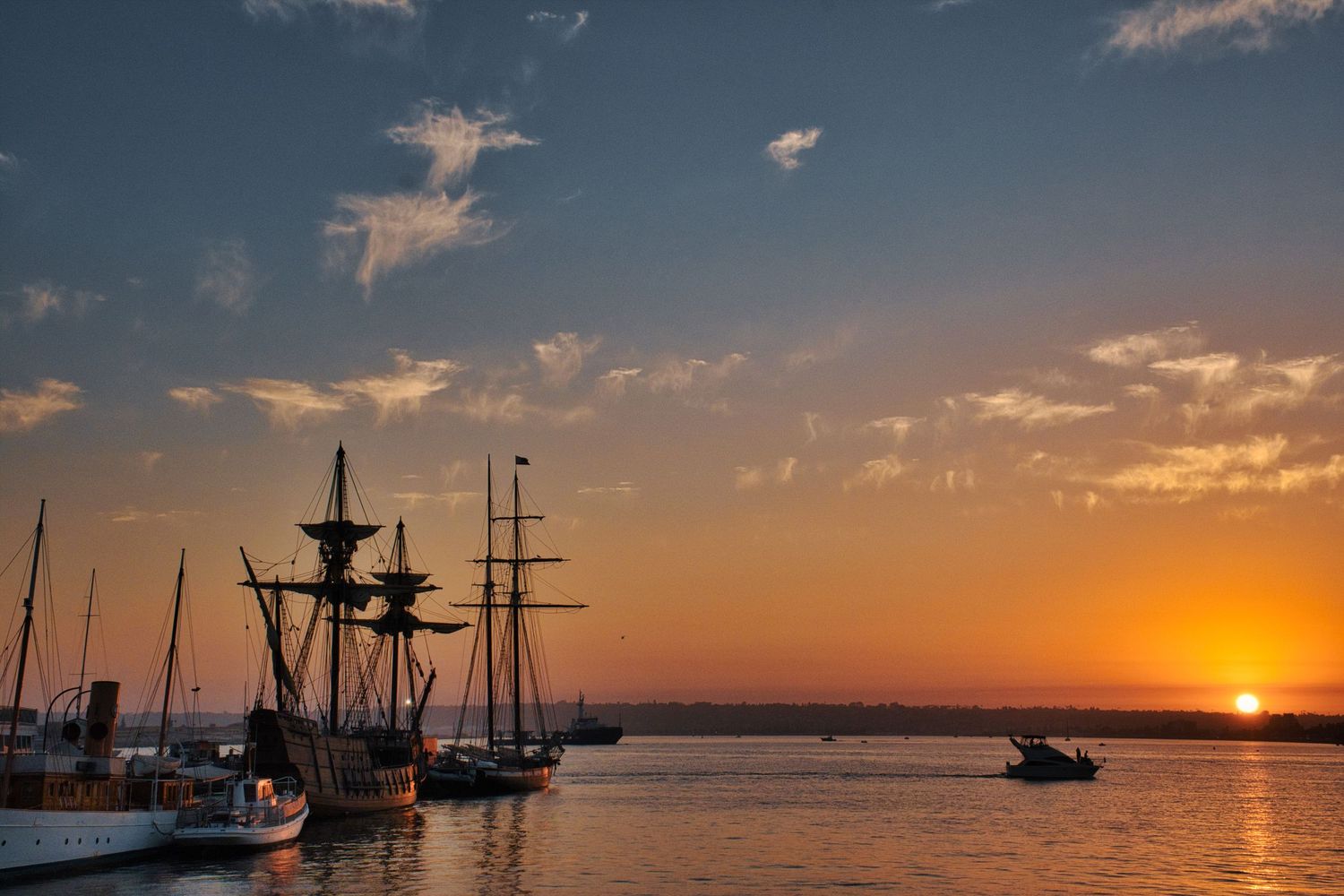 Harbor at sunset with silhouettes of sailing ships and boats on the horizon.