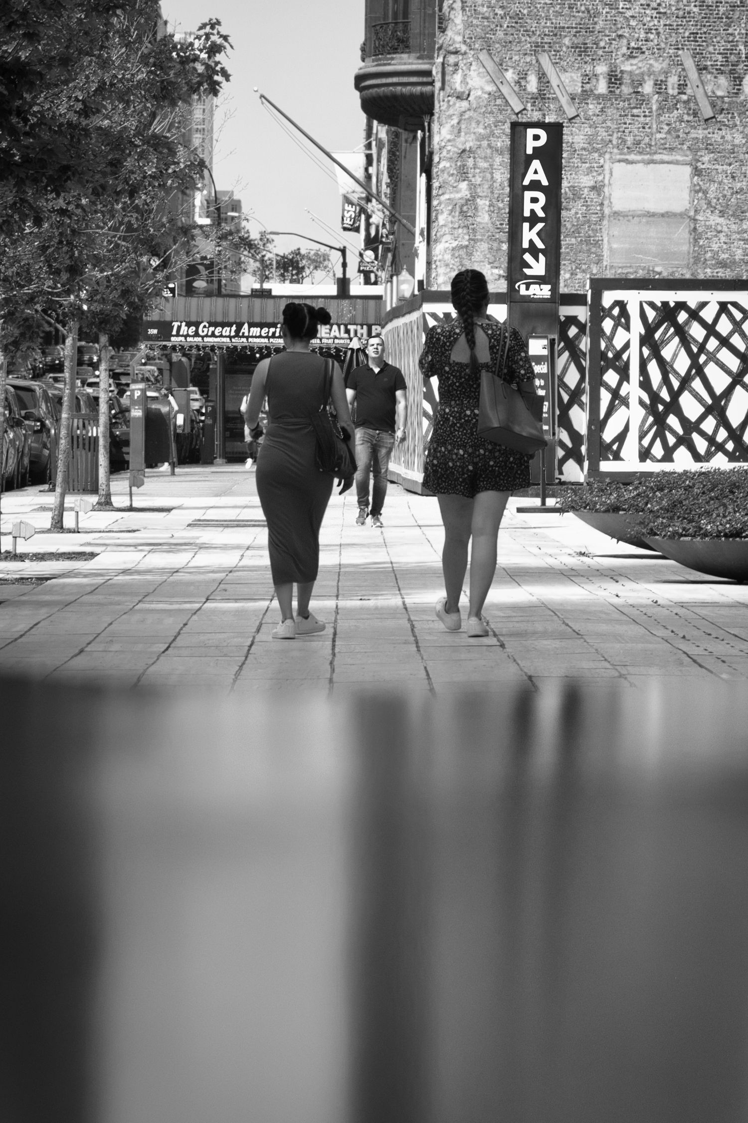 Black and white street scene showing people walking near urban buildings.