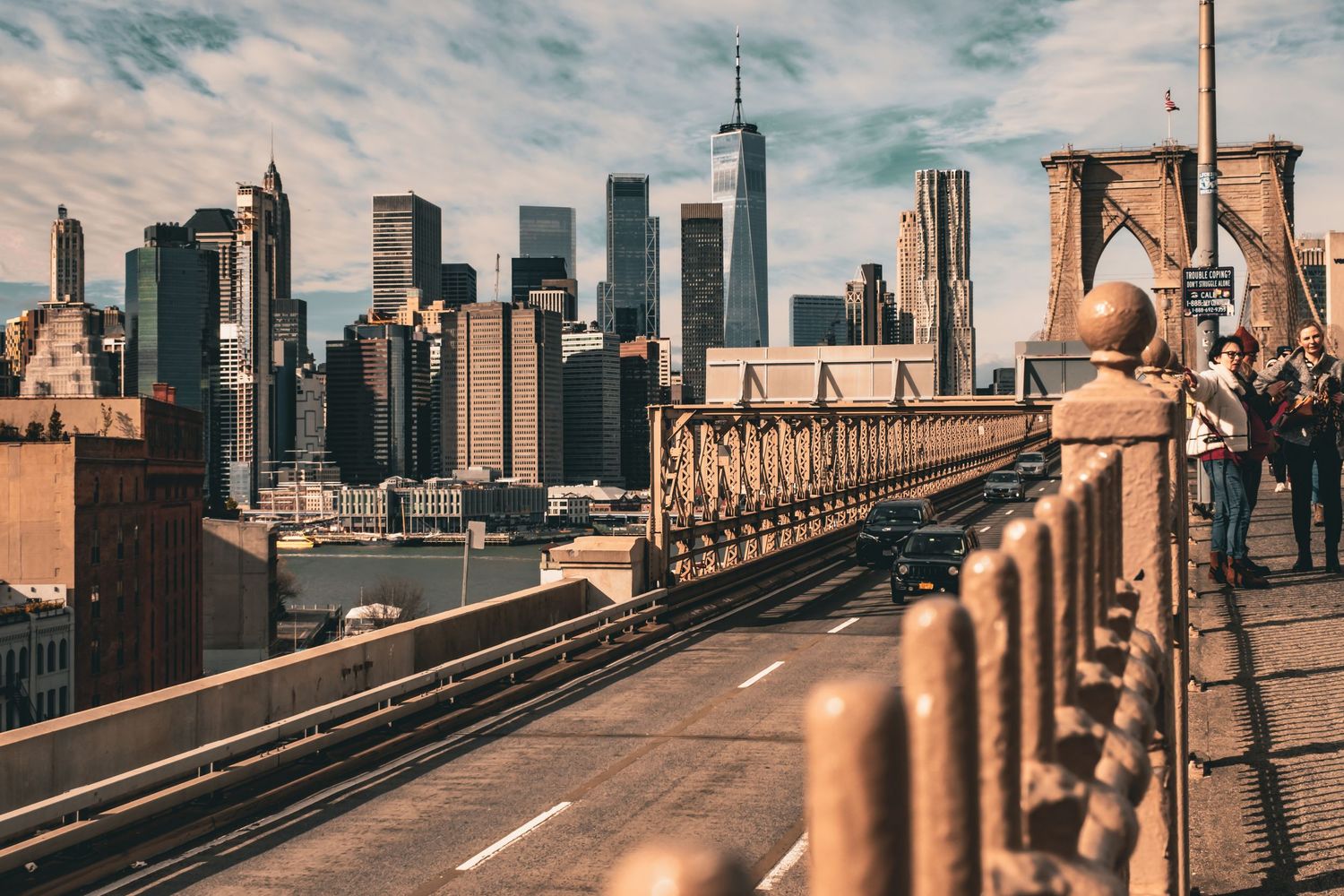 Brooklyn Bridge pedestrian path with Manhattan skyline visible in warm afternoon light.