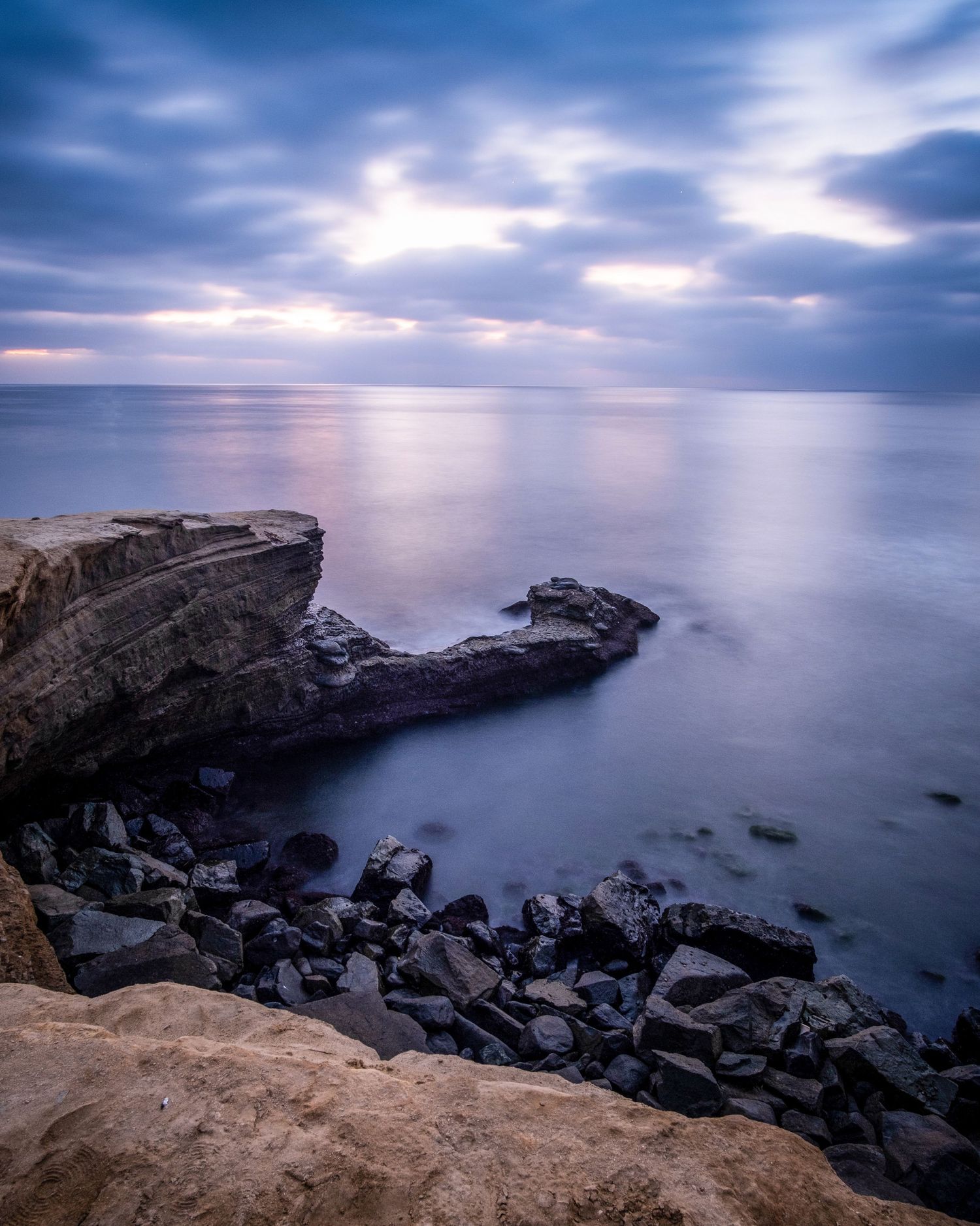 Rocky coastal landscape with dramatic cloudy sky over calm ocean waters.