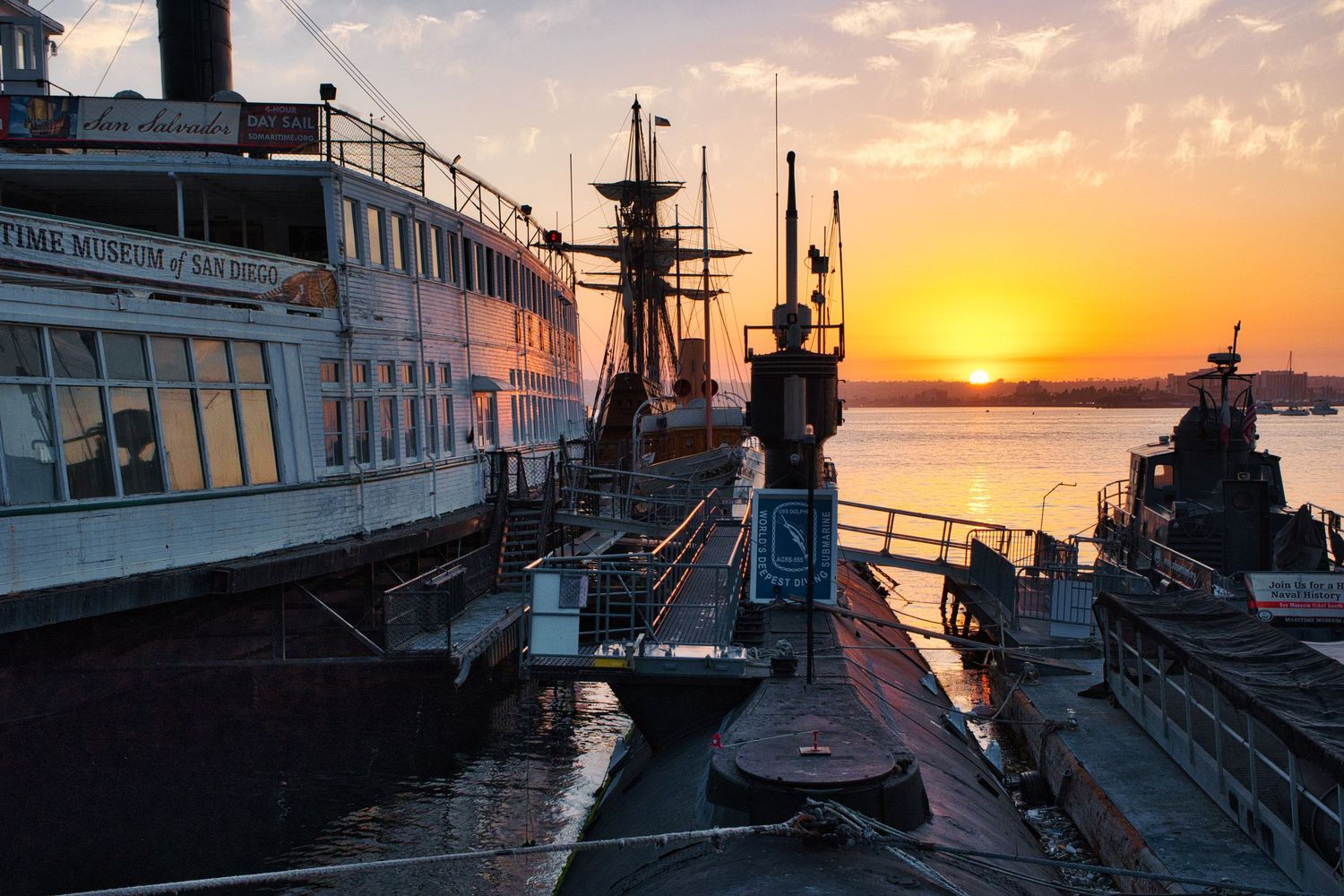 Scenic waterfront dock at sunset with boats and buildings silhouetted against an orange sky.