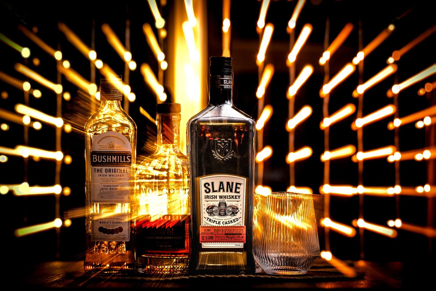 Illuminated whiskey bottles displayed against a dark background with dramatic light trails and bokeh effects.
