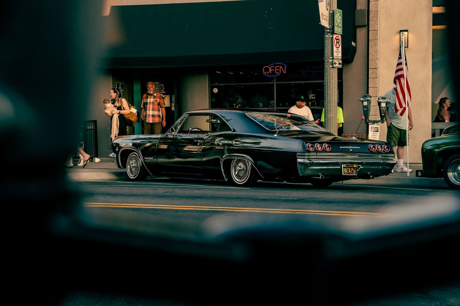 Classic black muscle car parked on urban street at dusk.
