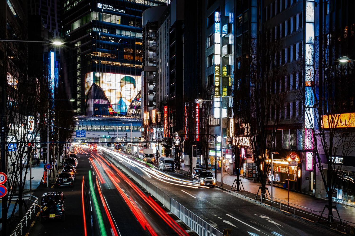 Long exposure night photography captures vibrant light trails from traffic on a busy urban street in Tokyo.